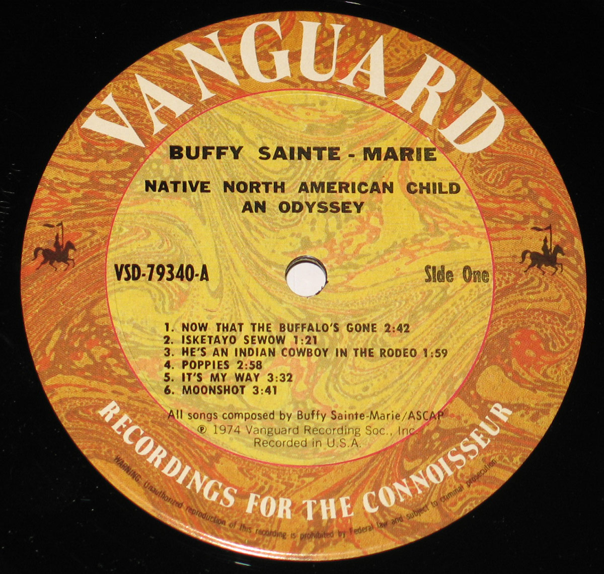 Close-up of the record label for Side One of 'Native North-American Child: An Odyssey' by Buffy Sainte-Marie. The label is rich with earthy tones of swirling orange, brown, and yellow, featuring a marbled texture. 'Vanguard' is emblazoned in bold, white capital letters across the top. The album title and artist’s name are printed in black, centered below. The tracklist for Side One, including six songs, is arranged neatly in a structured format. The label also contains small silhouetted figures of a horse and rider in each corner, adding a touch of traditional iconography. The words 'Recordings for the Connoisseur' curve along the bottom edge.