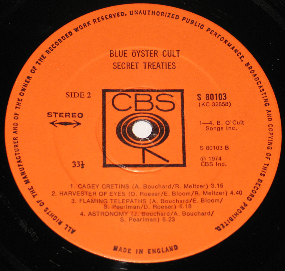 Blue Öyster Cult's 'Secret Treaties' vinyl record, pressed in England by CBS. The label is a striking deep orange, contrasting with the black vinyl. At the top, the band's name and album title are printed in bold black capital letters. Below them, 'Side 2' and 'STEREO' are aligned left, while the catalog number 'S 80103 (KC 32858)' is printed to the right. The CBS 'Walking Eye' logo dominates the center, with a thick black square enclosing the stylized eye. Around the label’s perimeter, small black text warns against unauthorized use. The tracklist features four songs, including 'Cagey Cretins' and 'Astronomy,' with writing credits and runtimes clearly marked. The bottom of the label states 'MADE IN ENGLAND' in capital letters, completing the official and classic CBS design.