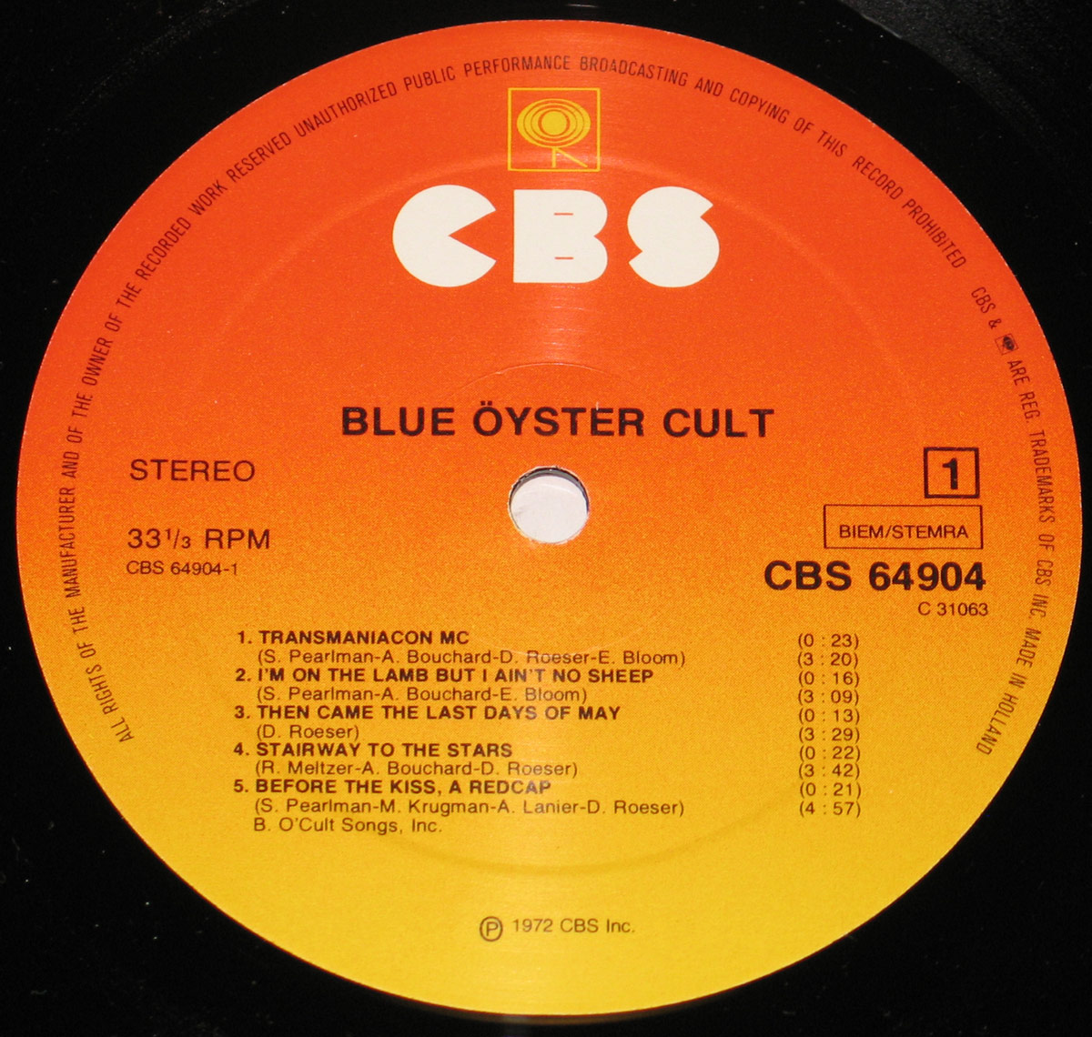 Close-up of the CBS record label on Blue Öyster Cult's self-titled album. The label has a striking orange-to-yellow gradient with the CBS logo in bold white letters at the top. The album title, 'Blue Öyster Cult,' appears in black uppercase font beneath the logo. The tracklist for Side 1 is printed in a clean, structured layout, detailing song titles, durations, and songwriting credits. Additional information includes the catalog number CBS 64904, BIEM/STEMRA rights management, and a copyright notice for 1972 CBS Inc. A centered spindle hole cuts through the label, adding to the classic vinyl aesthetic.