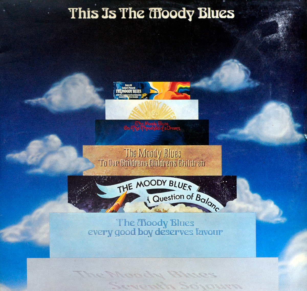 Album cover of 'This Is The Moody Blues' (1974). The artwork features a surreal design with seven stacked album covers forming a staircase against a dreamy, cosmic sky. Each album cover is a past release by The Moody Blues, leading up to the top, where 'Days of Future Passed' is partially visible. The background consists of deep blue hues and soft, white clouds, enhancing the celestial feel.