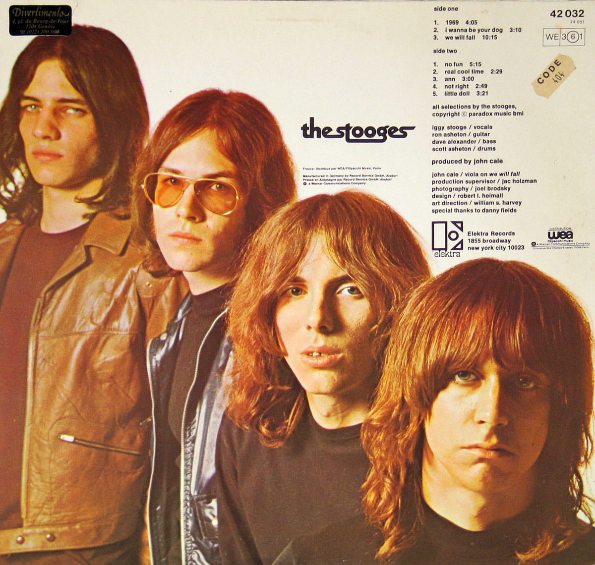 Back cover of The Stooges' self-titled album, featuring a band portrait with a plain white background. The tracklist is on the right side, along with credits. The band members stand in a staggered formation: Ron Asheton in a brown leather jacket, Dave Alexander in tinted glasses and a black leather vest, Scott Asheton with wavy hair, and Iggy Pop in the front with a blank stare and long bangs. The Elektra Records logo is visible at the bottom.