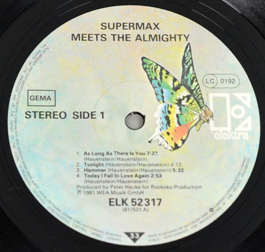 Close-up of Side One record label from 'Supermax - Meets Almighty'. Features a light, cloudy background with Elektra's iconic multicolored butterfly logo on the right. Black text lists the album title, track names, and catalog number ELK 52317. 'Stereo Side 1' is printed prominently alongside the GEMA rights society logo.