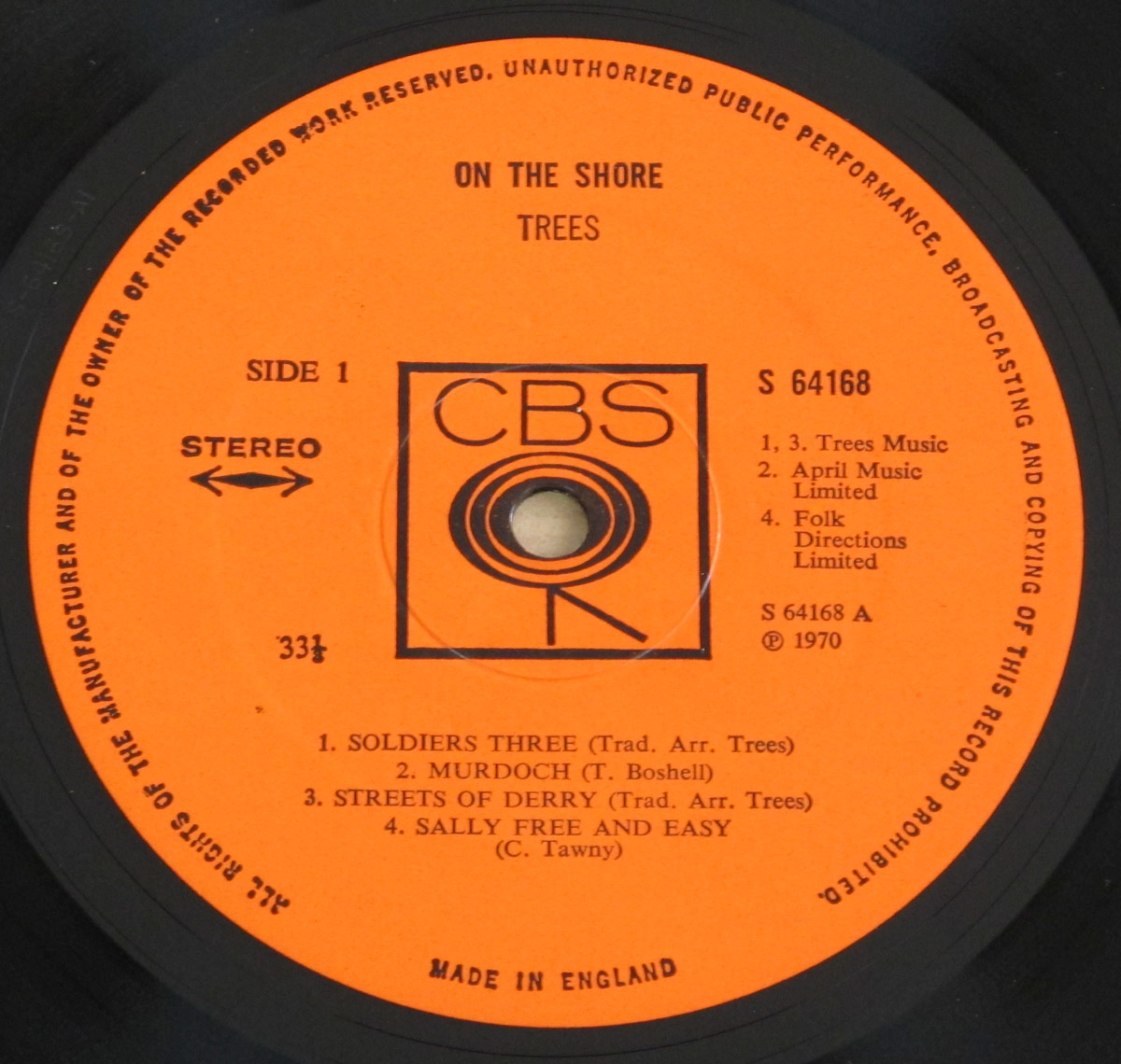 Close-up of the 'On The Shore' album label by Trees, pressed on CBS Records. The label is bright orange with bold black text, featuring the CBS logo in the center, a large black circle with concentric rings and the letters CBS above it. The text includes 'On The Shore' and 'Trees' at the top, with track listings for Side 1 below. The label also states 'STEREO' with arrows pointing both ways and '33⅓ RPM' at the bottom. The record's catalog number, S 64168, is printed on the right.