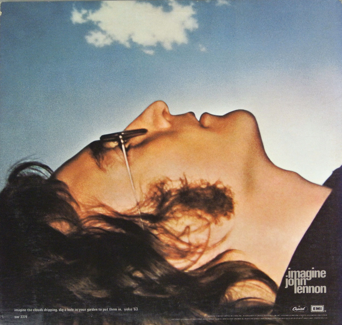 Back cover of John Lennon's 'Imagine' album. A striking photograph of Lennon lying on his back, head tilted upward, against a vast blue sky with a single small cloud. He wears his signature round glasses, which reflect light. The lower corner contains a Yoko Ono quote in small white text.