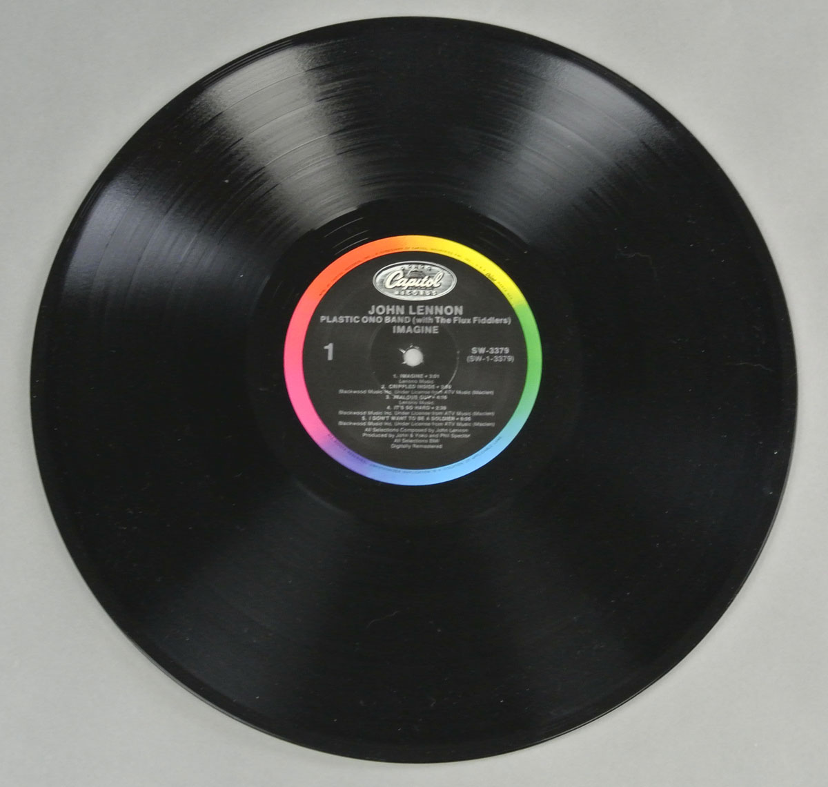 Vinyl record of John Lennon's 'Imagine' album, Side One. The black disc features a Capitol Records label at the center with a multicolored border. The text on the label includes the album title, artist name, tracklist, and catalog number SW-3379.