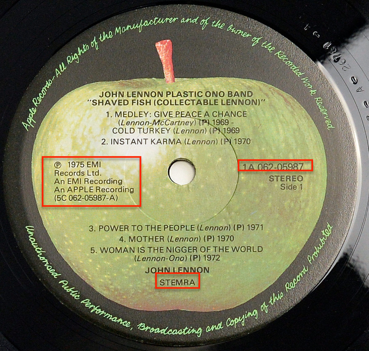 Close-up of the record label for John Lennon's 'Shaved Fish' album. The label features the iconic Apple Records logo, with a green apple at the center. The album title, tracklist, and copyright details are printed in black text, along with catalog numbers and the 'STEMRA' rights organization marking.