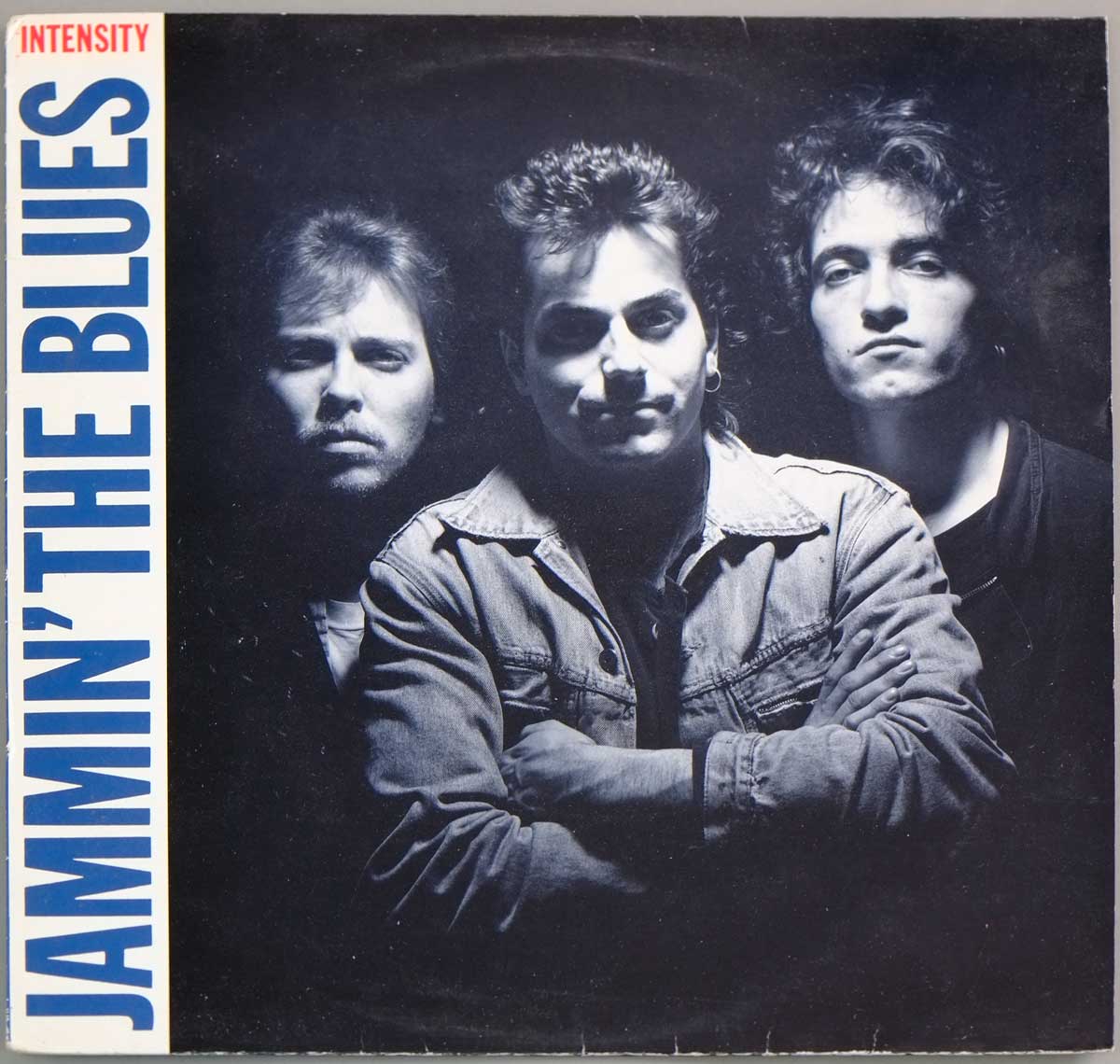 Front cover of JAMMIN' THE BLUES - Intensity album showing a black-and-white photo of three band members with bold blue vertical text on the left and the word INTENSITY in red.