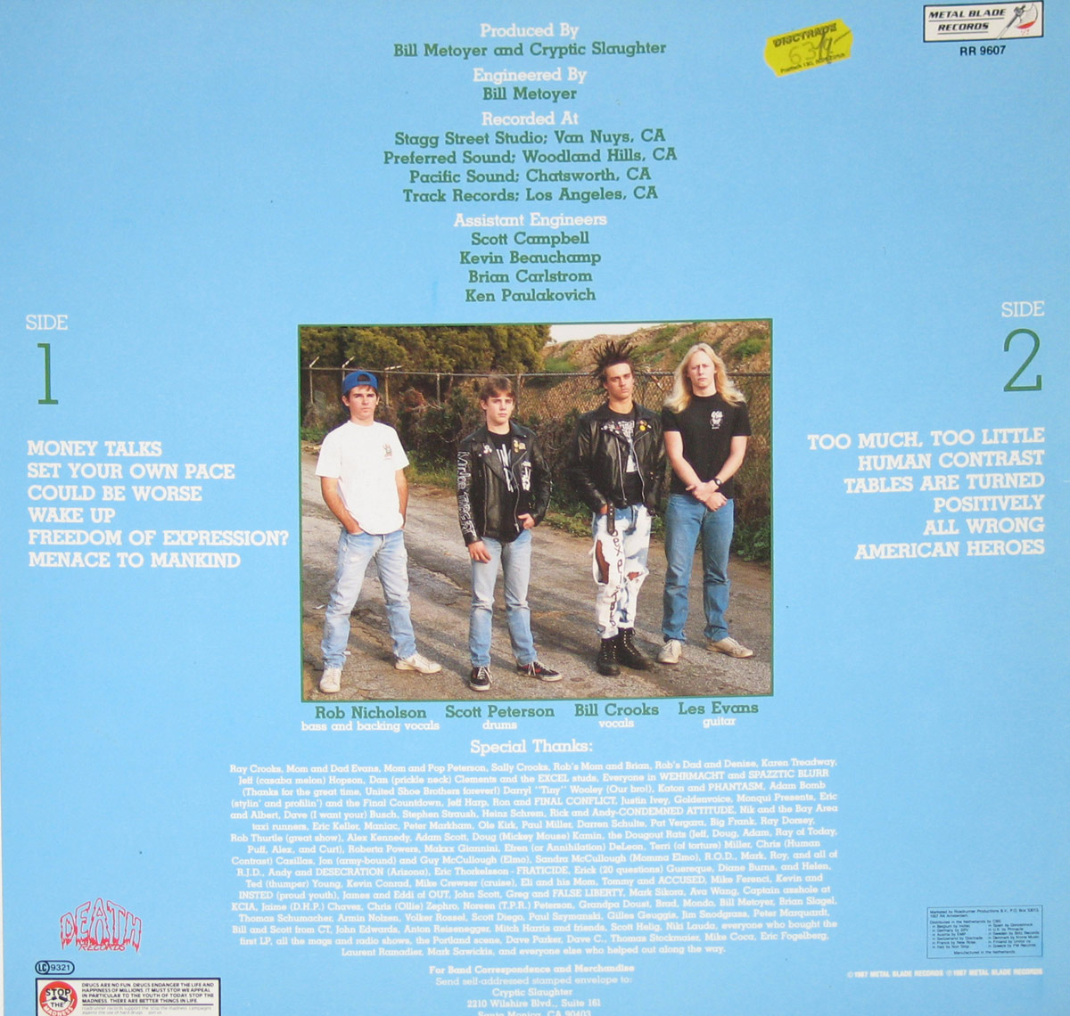 Back cover of CRYPTIC SLAUGHTER - Money Talks. Features a band photo of four members standing on a worn asphalt road with a chain-link fence behind them. The tracklist is split into two sections for Side 1 and Side 2, with song titles in bold white font against a blue background. Production credits, assistant engineers, and special thanks are listed at the top and bottom.