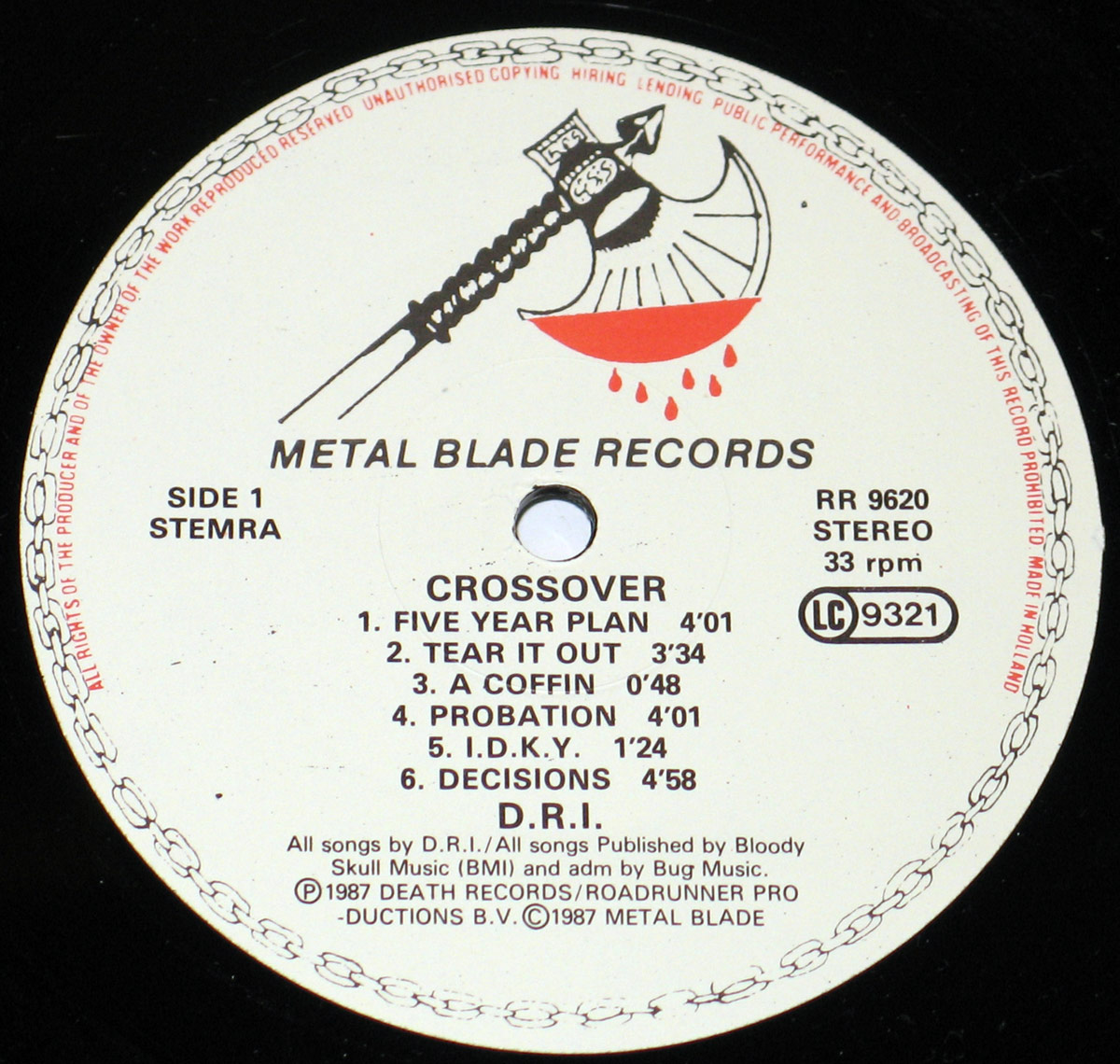 Close-up of the Side One record label from D.R.I.'s 'Crossover' (1987) vinyl LP, released under Metal Blade Records. The label is predominantly white with black text and features the iconic Metal Blade Records logo—a double-headed battle axe dripping with red blood. The circular border is adorned with a chain-like pattern. The text includes album details such as catalog number RR 9620, Stereo format, 33 rpm speed, and track listings: 'Five Year Plan,' 'Tear It Out,' 'A Coffin,' 'Probation,' 'I.D.K.Y.,' and 'Decisions.' Publishing credits and copyright information for Death Records, Roadrunner Productions, and Metal Blade Records (1987) are also present.