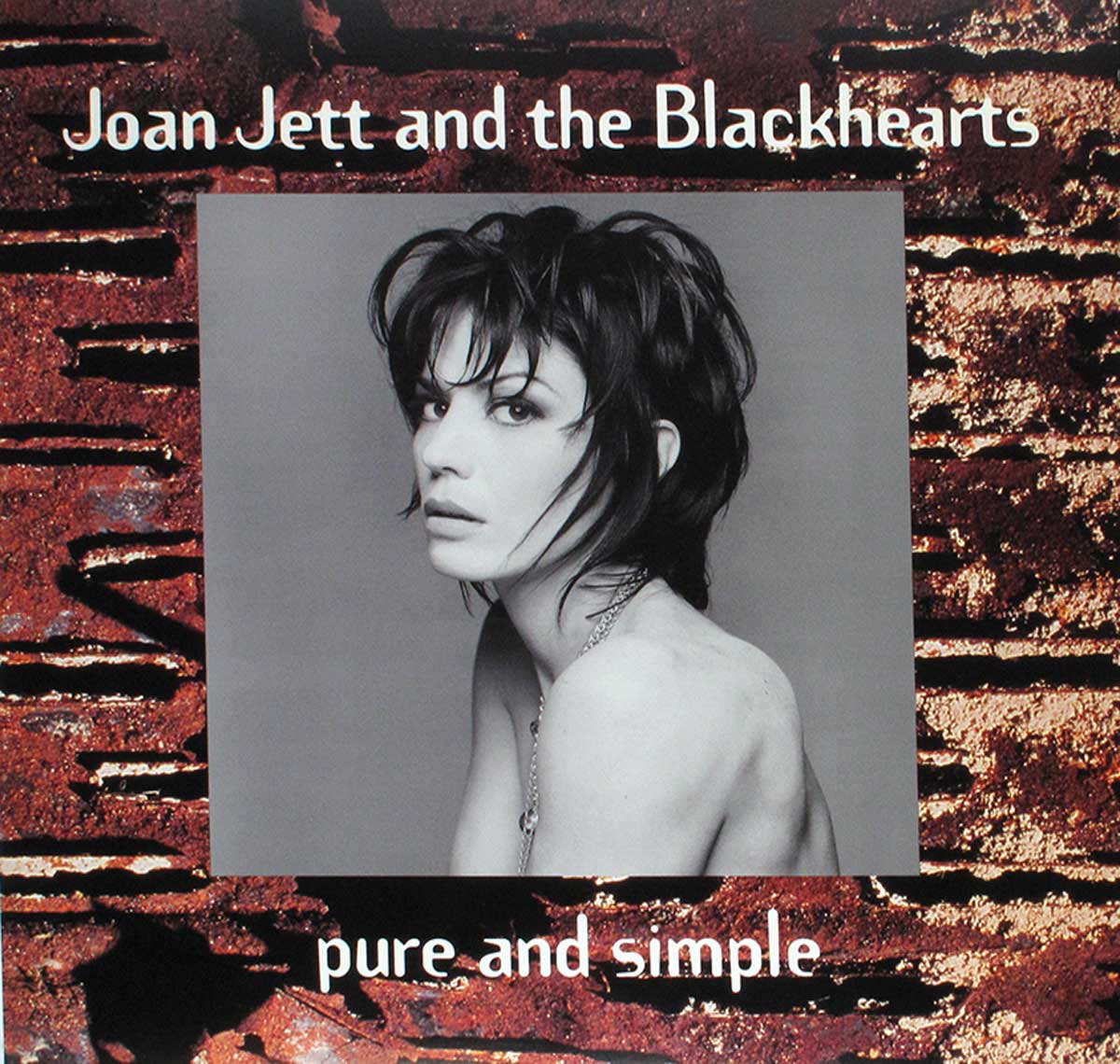 The photo shows a black and white nude Joan Jett portrait photo on a brick wall background 