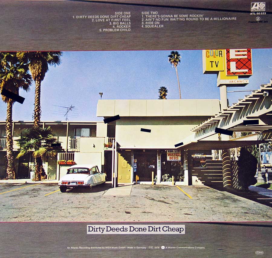 AC/DC Dirty Deeds Done Dirt Cheap album back cover. Shows a wide view of a 1970s motel scene with a Citroen DS car parked in front, palm trees, and empty parking spaces. The tracklist is displayed at the top, divided into Side One and Side Two. Black bars are placed over parts of the image, adding a sense of mystery. The AC/DC logo and Atlantic Records catalog information appear in the upper-right corner, with the album title at the bottom. 