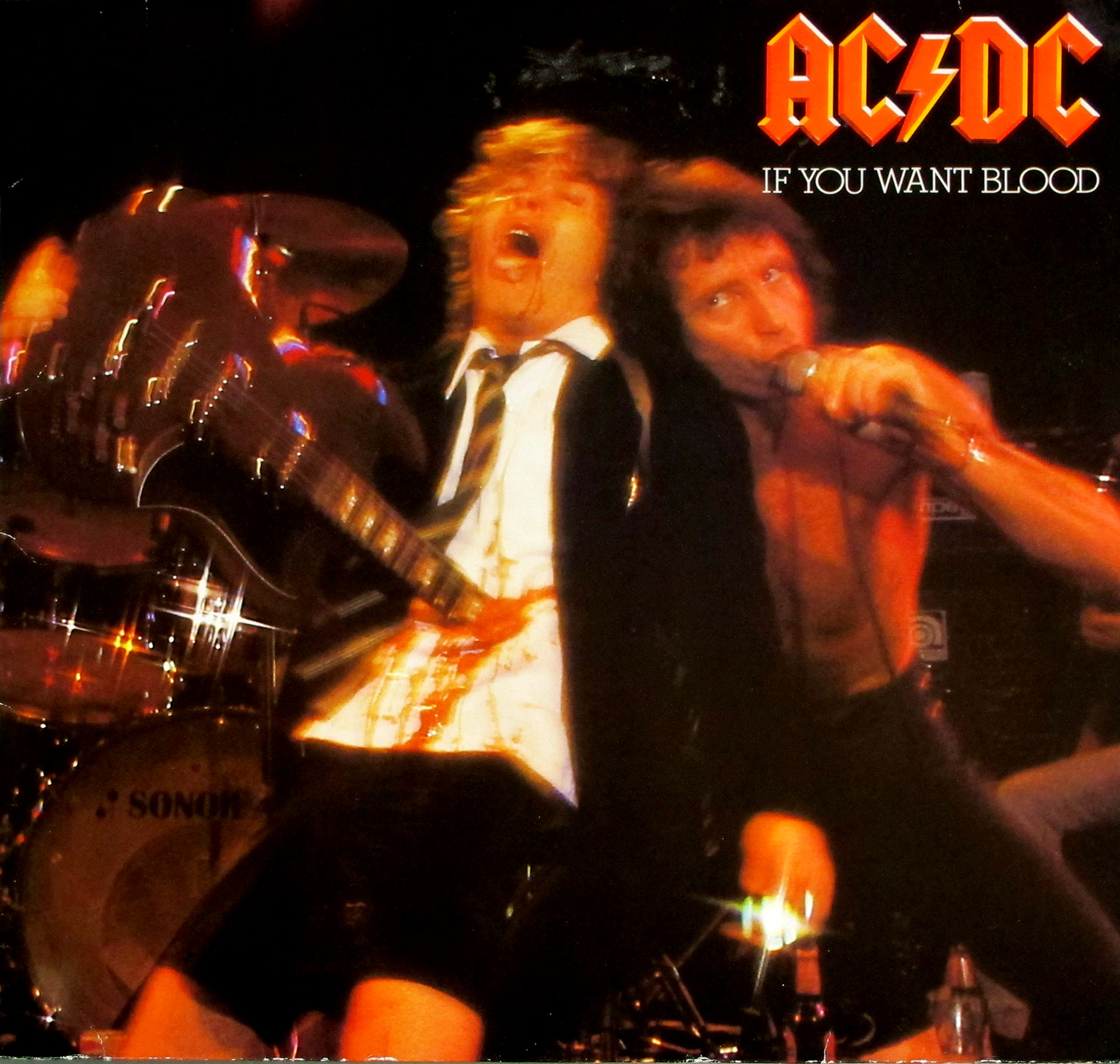 AC/DC If You Want Blood You’ve Got It album cover featuring Angus Young in a schoolboy outfit appearing impaled by his guitar, with Bon Scott singing shirtless into a microphone during a live performance.
