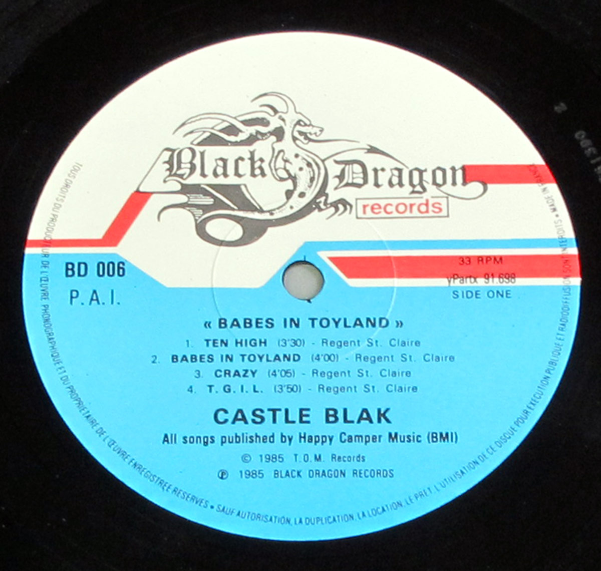 Close-up of Castle Blak’s Babes In Toyland Side One vinyl label on Black Dragon Records, blue and white design with red stripes, catalog BD 006, listing four tracks and publishing credits.