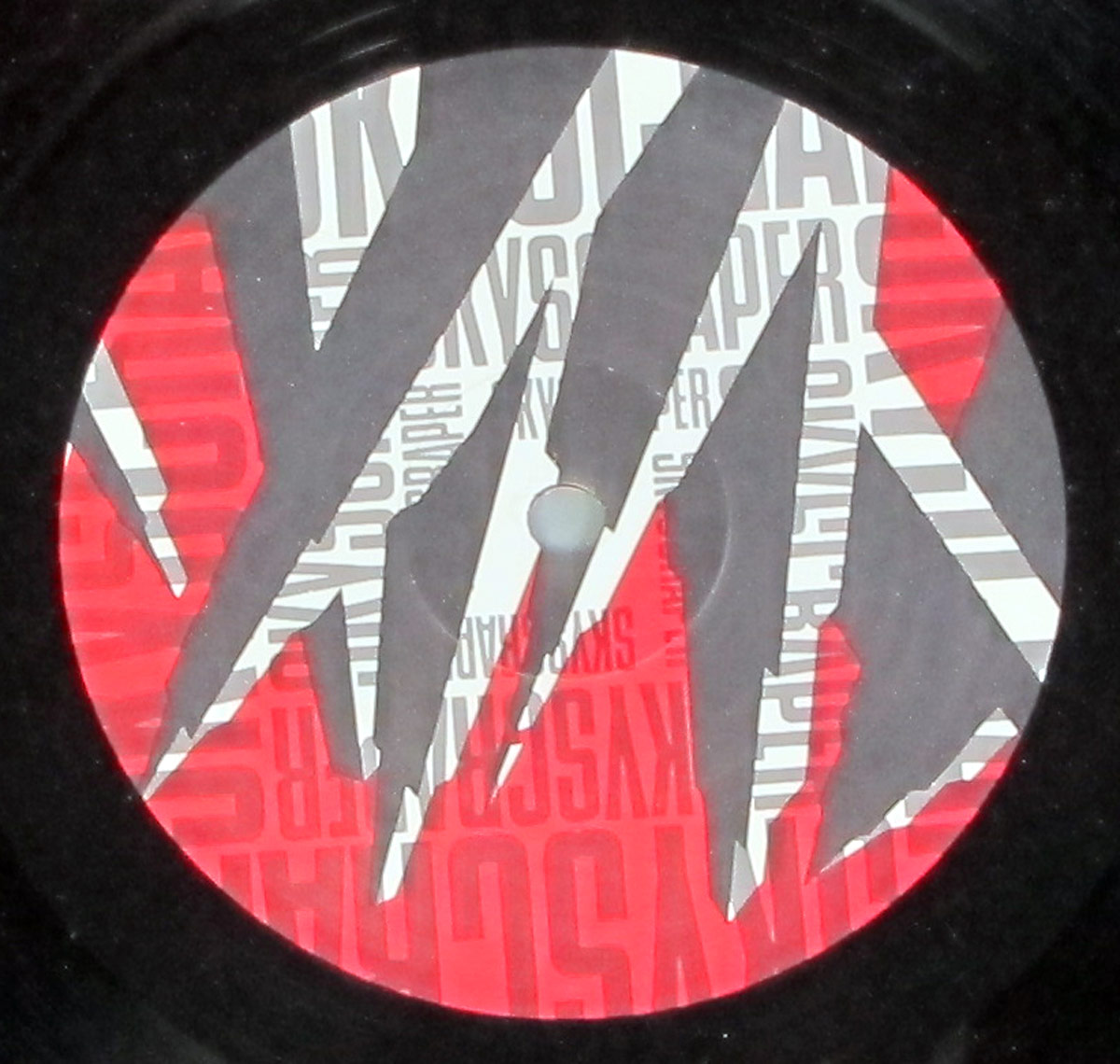 David Lee Roth's Skyscraper vinyl record label design featuring a repeat of the album title in grayscale and red, with jagged black mountain-like shapes cutting across the circular label.