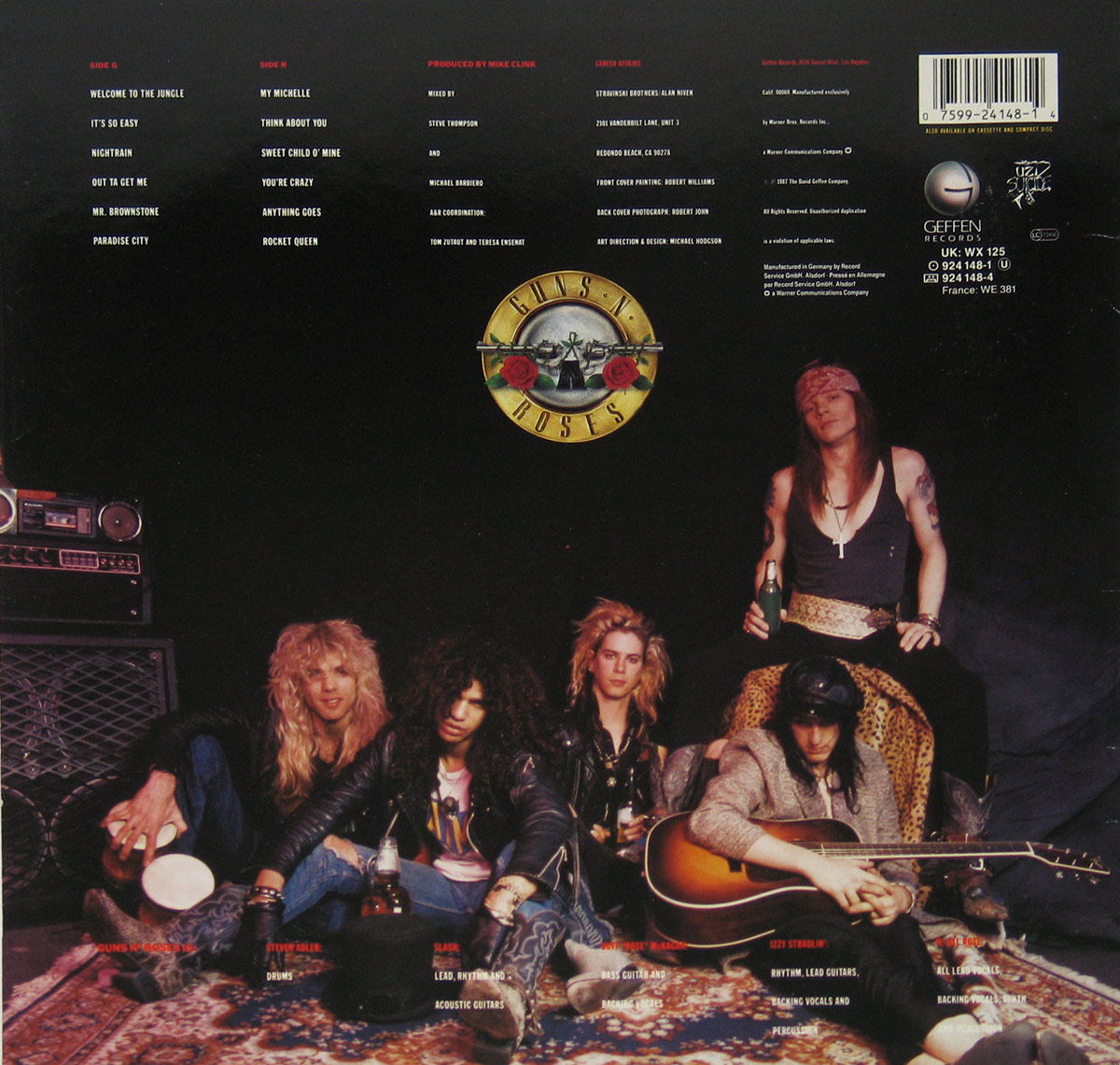 Back cover of Guns N’ Roses Appetite for Destruction album featuring a group photo of the band. From left to right: Steven Adler sits by an amplifier holding a drink, Slash sits cross-legged wearing a leather jacket, Duff McKagan gazes at the camera with tousled blonde hair, Izzy Stradlin holds an acoustic guitar while wearing a hat, and Axl Rose reclines above the group with a bandana and leopard-print pants, holding a bottle. The iconic Guns N’ Roses logo with crossed guns and roses is displayed above them