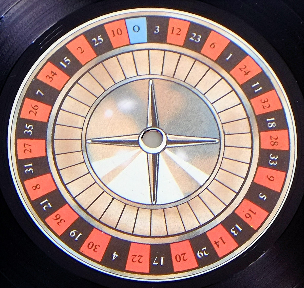 The label of 'No Va Más' by Barón Rojo is designed as a highly detailed roulette wheel, complete with alternating red and black numbered pockets, a single blue '0' pocket, and a metallic gold center with a compass-like design. The grooves of the vinyl record surround the label, adding depth and realism to the casino-themed aesthetic.