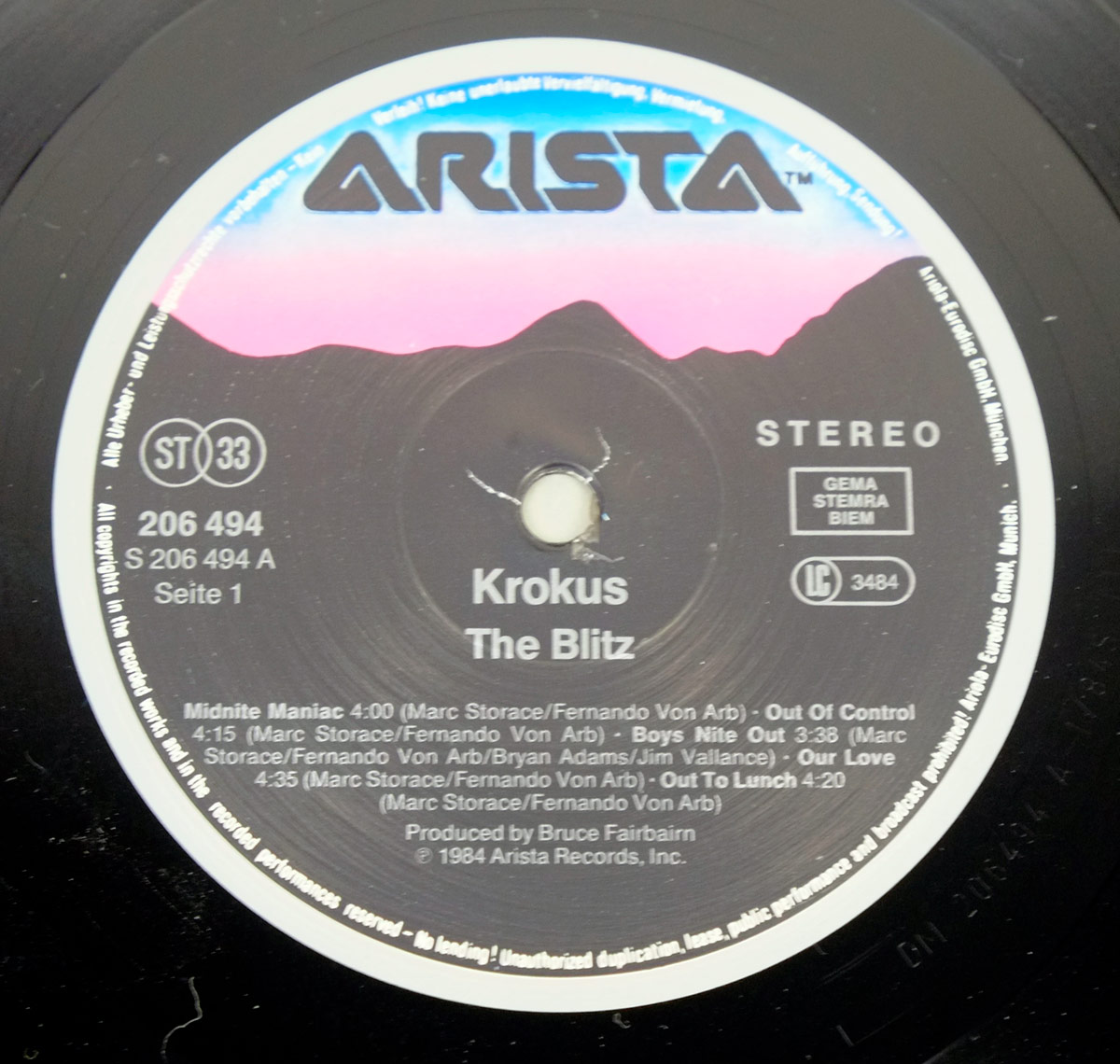 KROKUS 'The Blitz' record label on Side 1 of the 1984 Arista LP, showing tracklist, songwriting credits, catalog number 206 494, and producer Bruce Fairbairn. Features Arista logo with blue-pink mountain graphic.