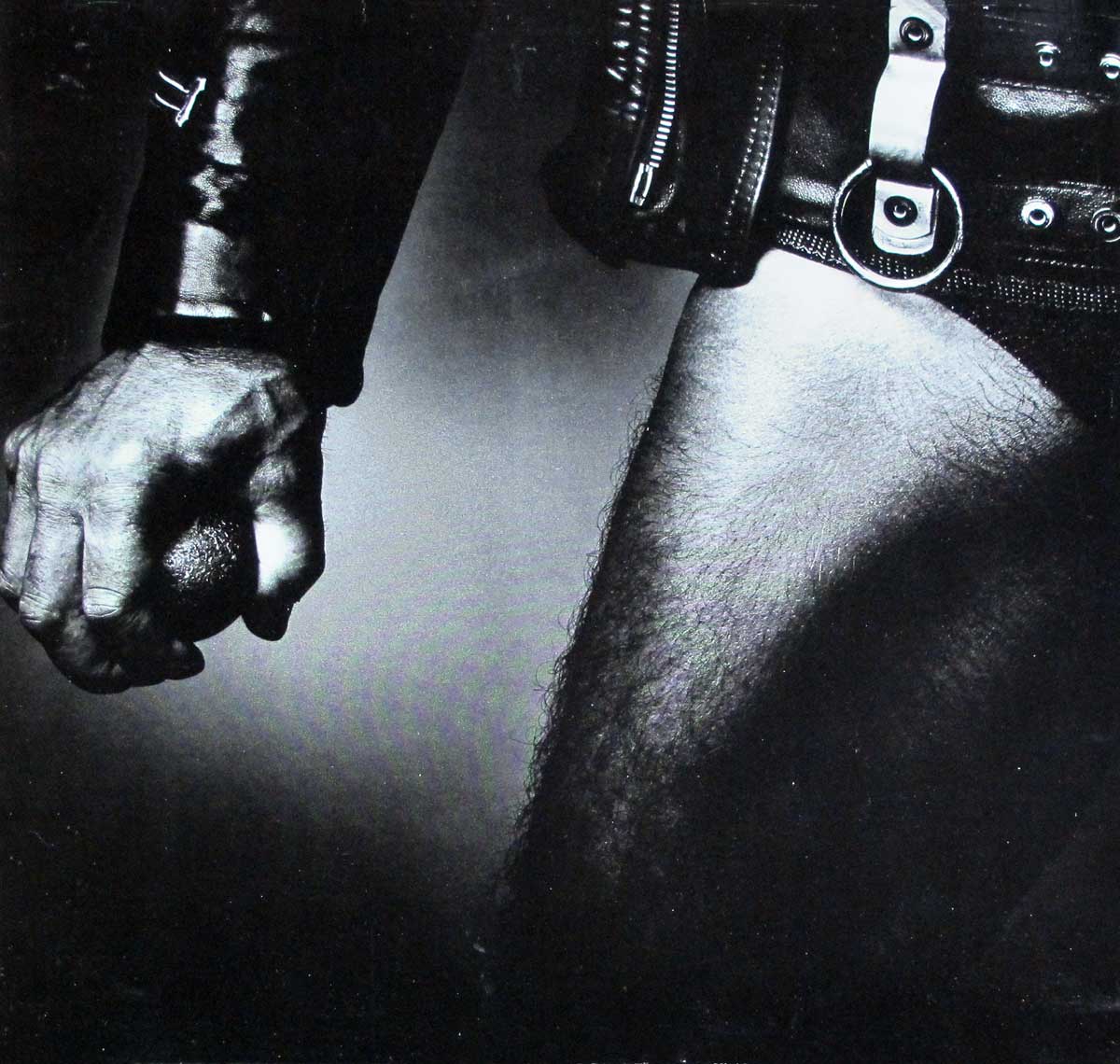 Close-up black-and-white album cover featuring a man in leather attire gripping a textured ball, symbolizing strength, rebellion, and the raw energy of heavy metal music.