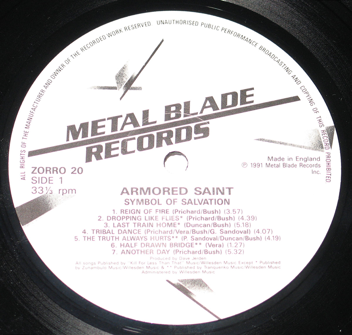 Close-up of the record label on Side 1 of Armored Saint's 'Symbol of Salvation' vinyl LP. The label is white with black text and features the Metal Blade Records logo at the top, consisting of a stylized sword. Below, the album title, band name, and tracklist for Side 1 are displayed, along with copyright and production credits. The catalog number 'ZORRO 20' and '33 ⅓ rpm' speed information are also included.