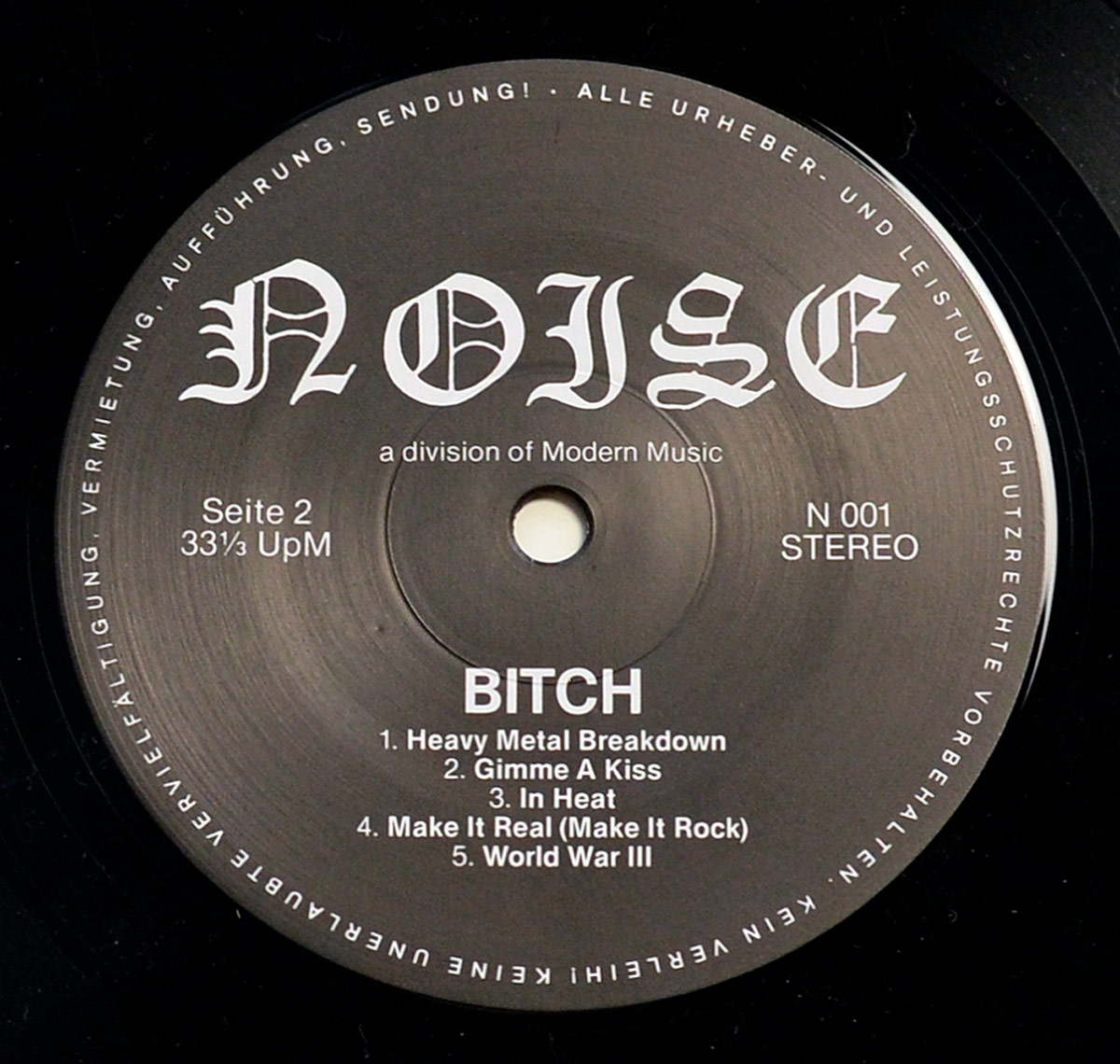 Close-up of Side Two label of BITCH - Be My Slave vinyl LP. The black label features the NOISE Records logo in gothic font, track listing for Side Two: 'Heavy Metal Breakdown,' 'Gimme A Kiss,' 'In Heat,' 'Make It Real (Make It Rock),' and 'World War III.' The catalog number N 001 and stereo format are displayed.
