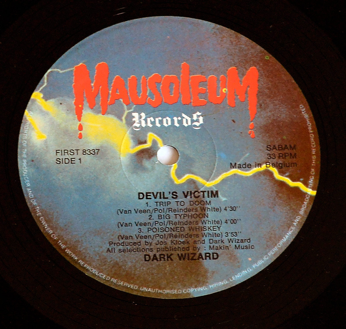 Side One record label of Dark Wizard's Devil's Victim EP, Mausoleum Records Belgium 1984. The label background features a cloudy sky with yellow lightning streaks. At the top, the Mausoleum Records logo is printed in bold red dripping letters, with 'Records' in white Gothic font below. Text details include catalog number FIRST 8337, Side 1, 33 RPM, SABAM rights society, and 'Made in Belgium'. Track list: Trip to Doom (4:30), Big Typhoon (4:00), and Poisoned Whiskey (3:53), with composers Van Veen, Pol, Reinders, White. Production credit: Jos Kloek and Dark Wizard. All selections published by Makin' Music. Band name printed at the bottom.