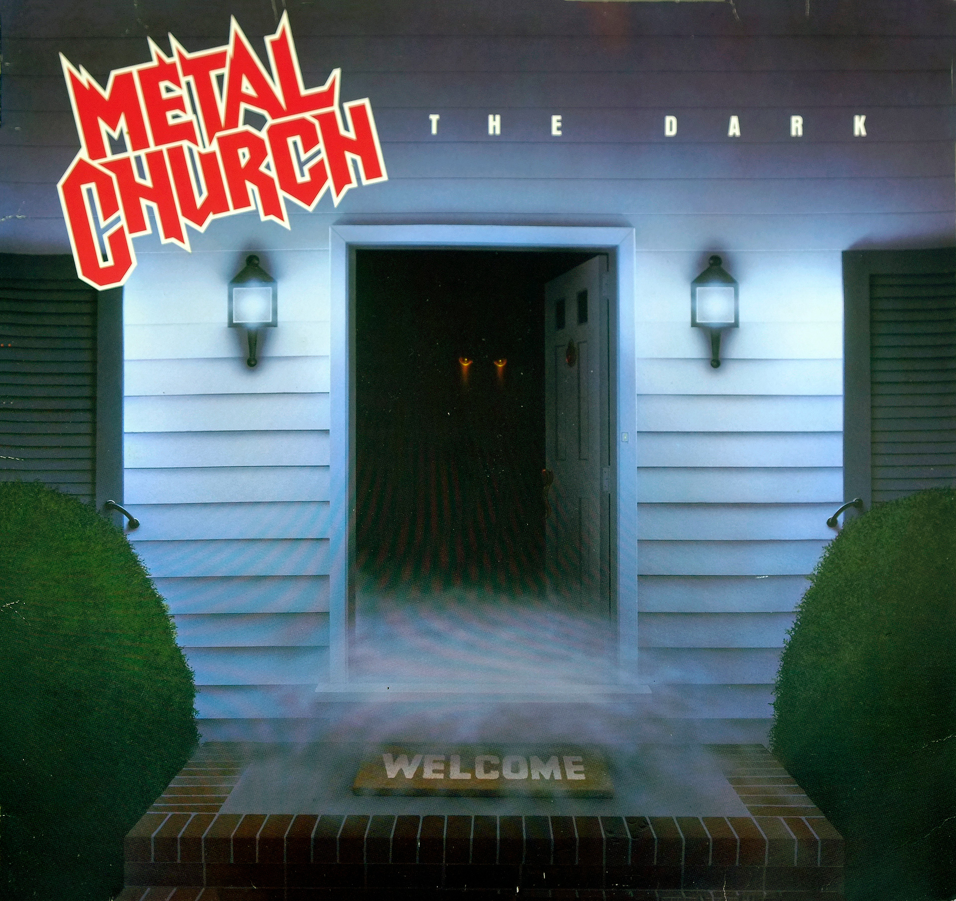 Metal Church The Dark album cover, showing a suburban home’s open doorway with glowing eyes in darkness, mist rolling across the steps, and a “Welcome” mat in front. Bold red-and-white band logo and album title in white.