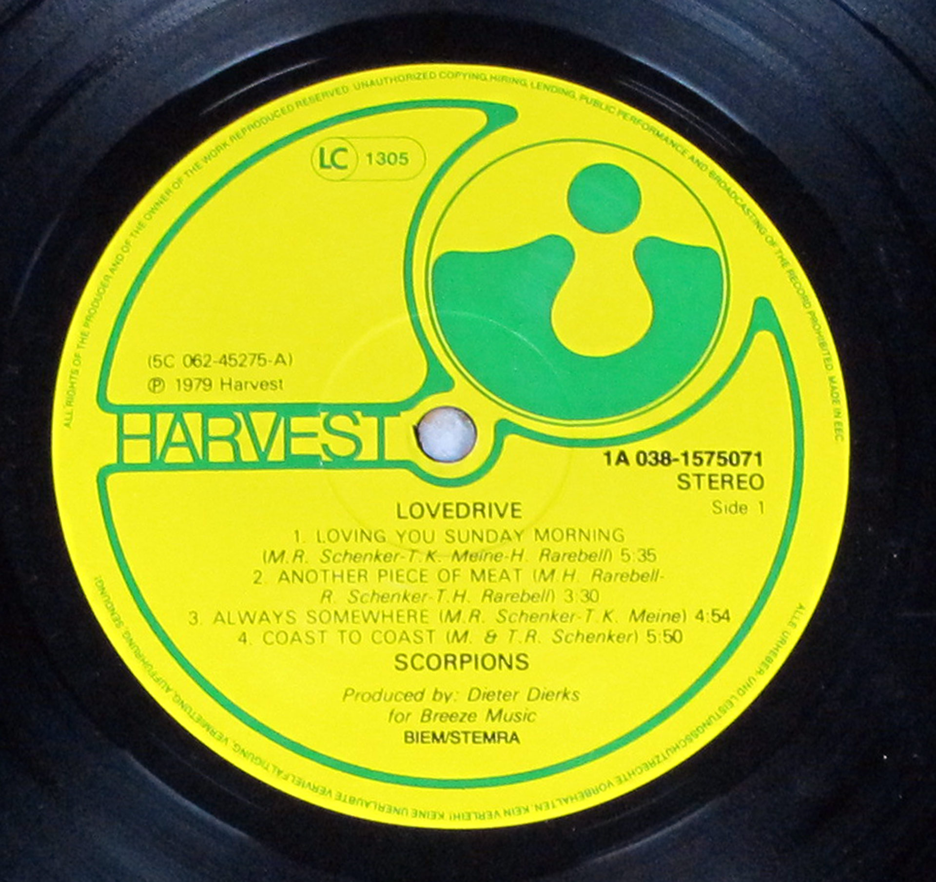 Close-up of the Side One record label for the Scorpions Lovedrive Netherlands Fame edition, pressed on the classic yellow Harvest label. The circular label displays the Harvest logo in green, featuring a stylized figure inside a rounded shape. Around the edges, fine print notes reproduction rights and manufacturing. The catalog number 1A 038-1575071 is printed clearly along with stereo designation. Track listing for Side One includes Loving You Sunday Morning, Another Piece of Meat, Always Somewhere, and Coast to Coast, with songwriting credits and durations. Producer credit for Dieter Dierks appears at the bottom, along with rights societies BIEM/STEMRA.