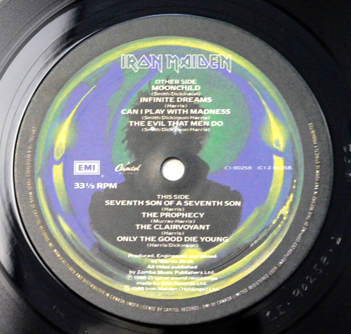 Iron Maiden's 'Seventh Son of a Seventh Son' vinyl record label featuring a dark, mystical background with green and blue hues, track listings for both sides, the band's name in bold metallic font, and EMI & Capitol Records logos.
