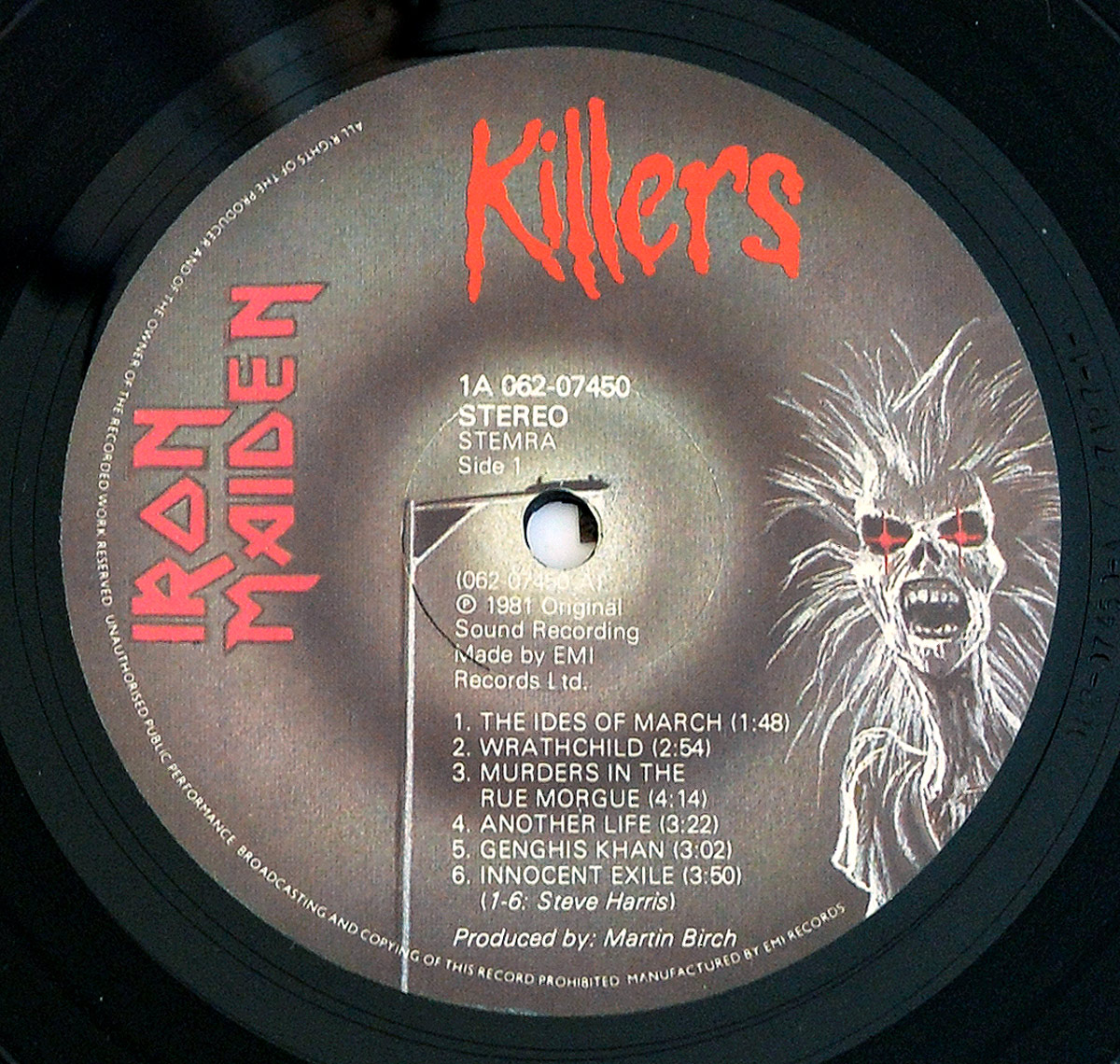 Close-up of the Side One label of Iron Maiden’s ‘Killers’ Netherlands pressing, showing the 1A 062-07450 catalog number, STEMRA rights society, and a grey/brown textured background with the Iron Maiden logo in red on the left. On the right is a screaming Eddie illustration with glowing red eyes and spiked white hair. The tracklist is printed in clean white text below the spindle hole, and rim text around the edge details broadcast and copying restrictions. Produced by Martin Birch and made by EMI Records Ltd.