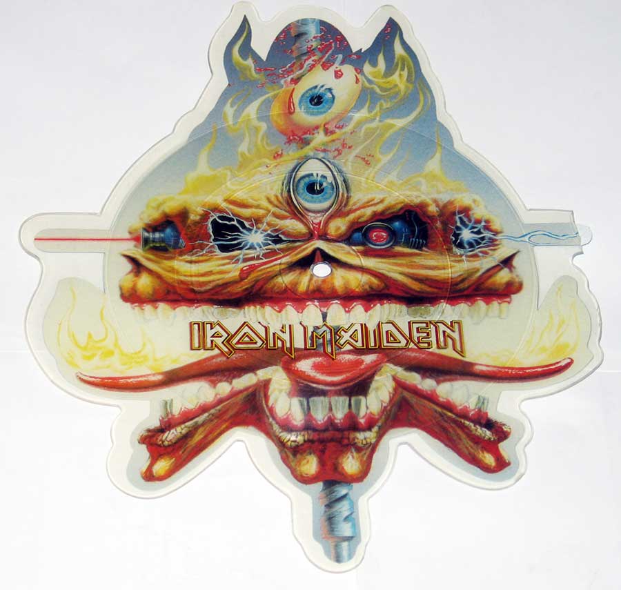 Cut-to-shape picture disc of Iron Maiden’s single The Clairvoyant, featuring Eddie with a fiery design, three eyes symbolizing prophecy, and elements of energy and flames, inspired by the “Seventh Son of a Seventh Son” album era.