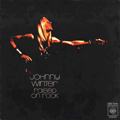 Album cover for Johnny Winter's 'Raised on Rock,' featuring a dark background with a warmly lit photo of Winter performing, arm extended, and minimalist text design