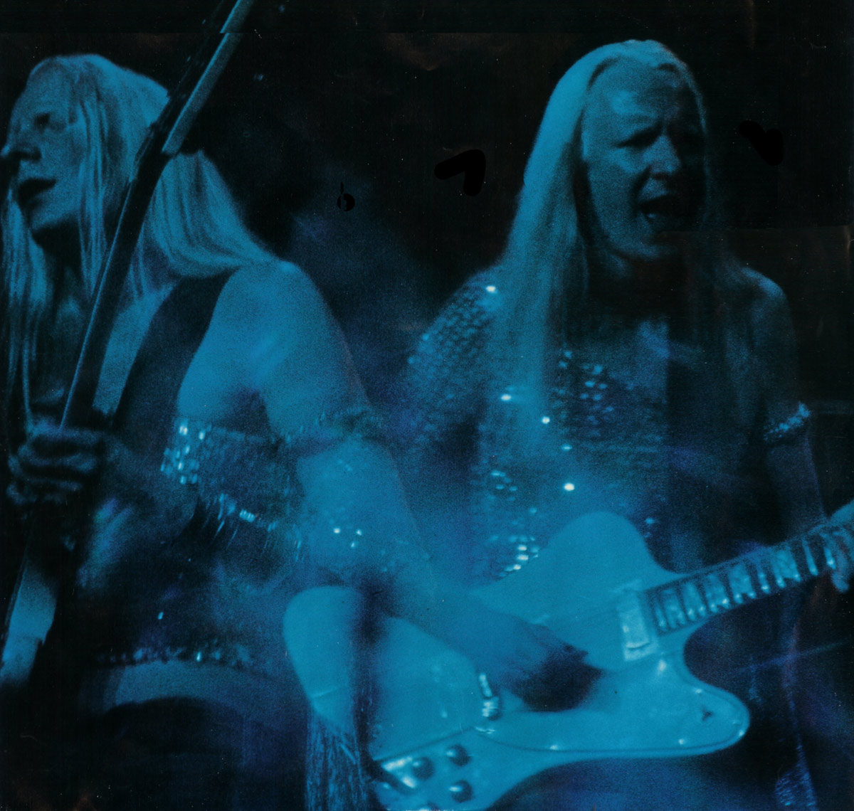 Blue-tinted live performance photo of Johnny Winter printed on the custom inner sleeve of 'John Dawson Winter III.' Two overlapping stage images show him singing and playing a white electric guitar under dark concert lighting. His long light hair hangs straight as he leans into the microphone, wearing a shimmering sleeveless top. The scene is grainy, high-contrast, and atmospheric.