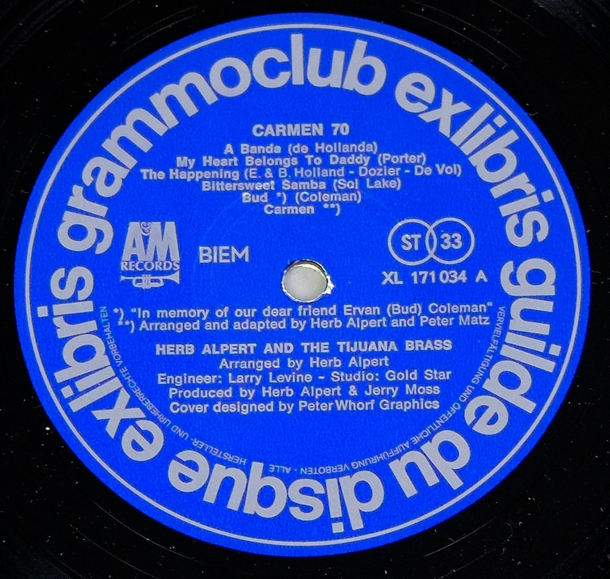 Close-up of Side A label from the 'Carmen 70' vinyl record by Herb Alpert & The Tijuana Brass. The label is deep blue with white text, featuring the Ex Libris and A&M Records logos, the tracklist, and production credits. A central spindle hole shows signs of wear.