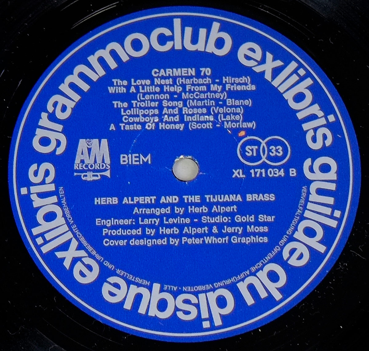 Close-up of Side B label from the 'Carmen 70' vinyl record by Herb Alpert & The Tijuana Brass. The label is deep blue with white text, featuring the Ex Libris and A&M Records logos, the tracklist for Side B, and production credits. The spindle hole at the center shows slight wear from use.