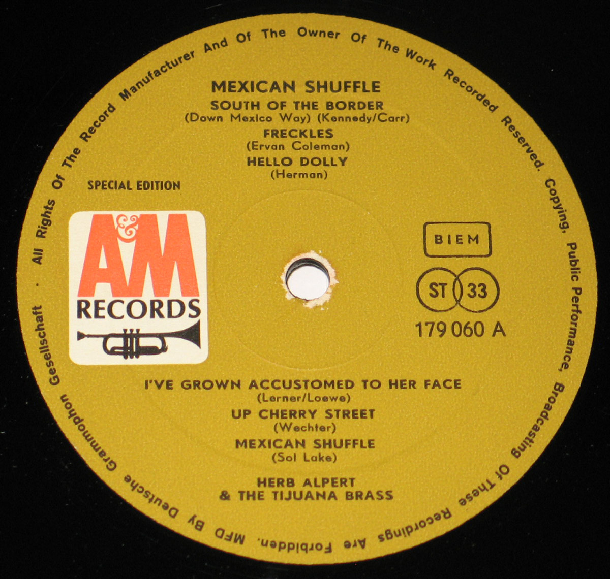 Close-up of Side One label of the 'Mexican Shuffle' vinyl record by Herb Alpert & The Tijuana Brass. The gold-colored label features the A&M Records logo, tracklist, and copyright text in black, with a centered spindle hole showing wear around the edges.
