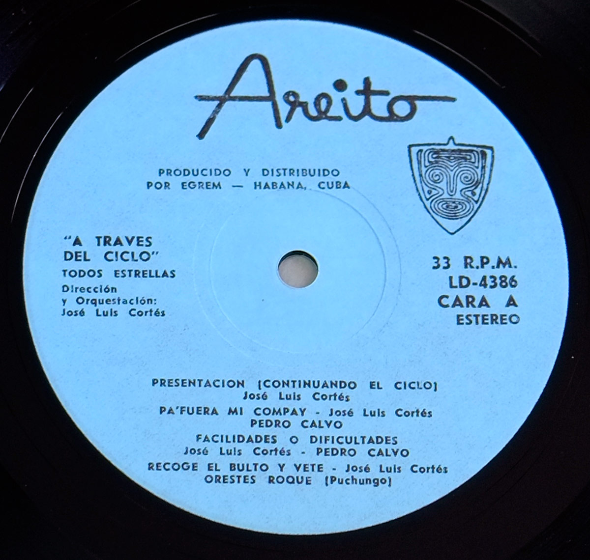 Close-up of the Areito record label on the vinyl LP ‘A Través del Ciclo’ by Todos Estrellas. The label features a sky-blue background with the classic handwritten Areito logo, EGREM distribution details, and a Taíno-inspired emblem. It lists track titles, artists like José Luis Cortés and Pedro Calvo, and the catalog number LD-4386. A vintage Cuban pressing from Havana’s legendary studios.