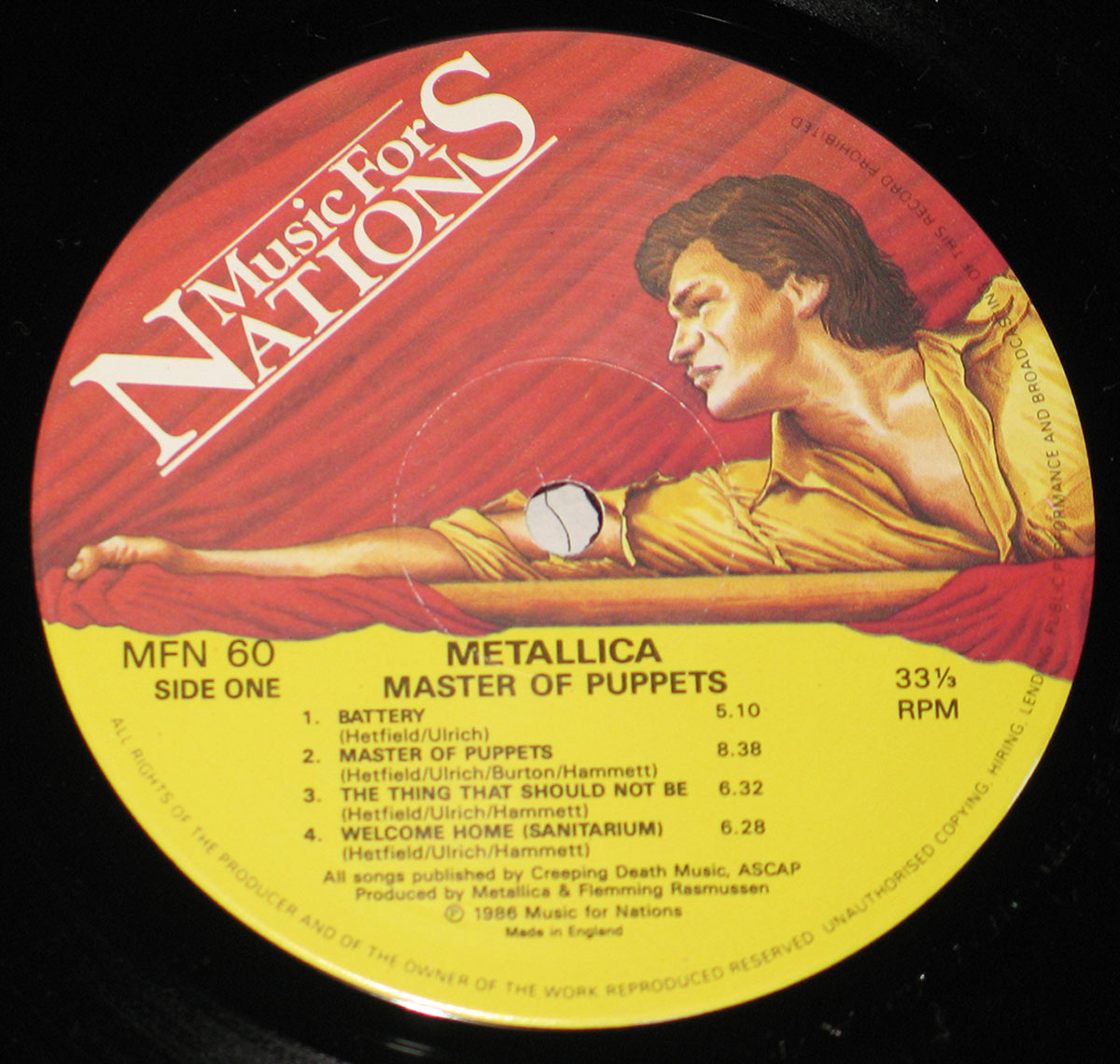 UK pressing of Metallica's 'Master of Puppets' Side One record label under Music For Nations. The label features an illustration of a man in a yellow shirt gripping a bar, set against red drapery. The lower yellow portion contains black text displaying the tracklist, MFN 60 catalog number, and production credits, with 'Made in England' noted at the bottom.