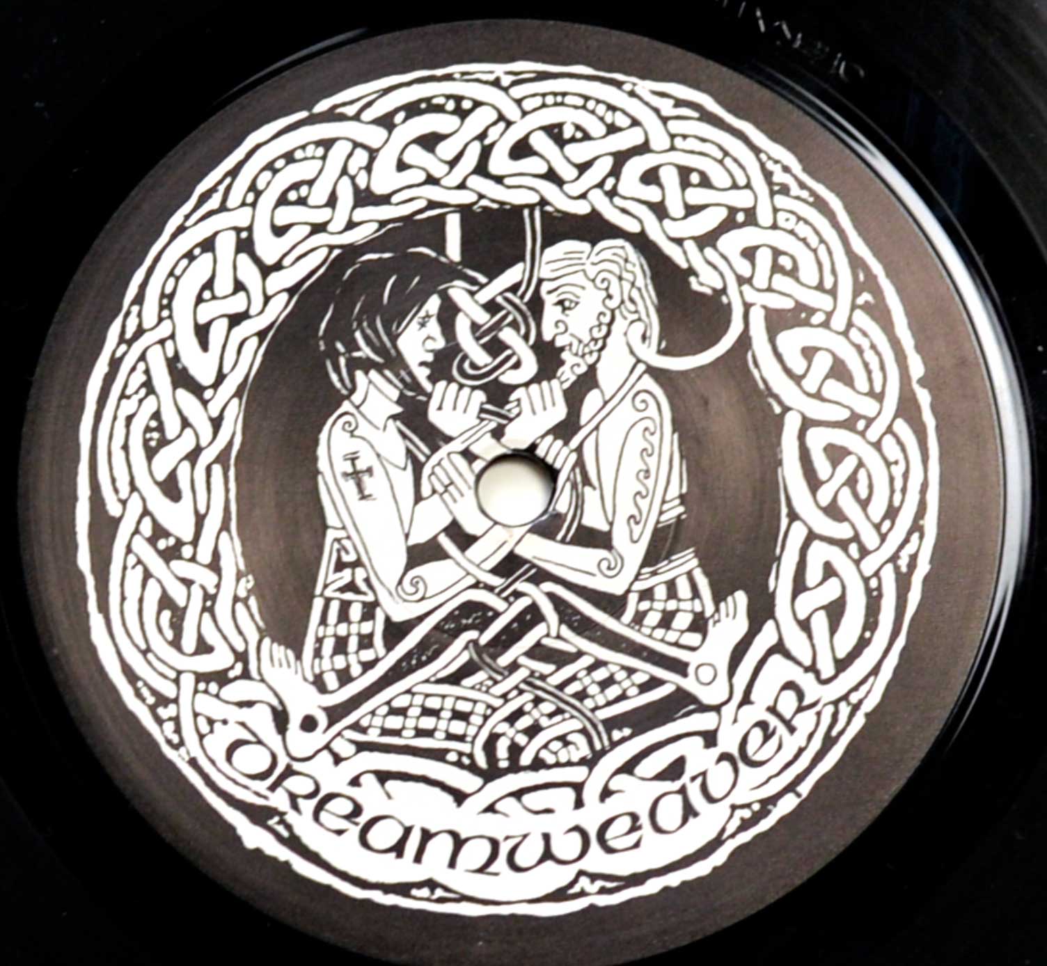 Record label artwork for Sabbat’s Dreamweaver album featuring a black-and-white Celtic-inspired design. The central illustration depicts a bearded male figure and a long-haired female figure facing each other, holding a knotted rope that connects them, symbolizing unity and mysticism. The scene is surrounded by an intricate circular Celtic knot border. At the bottom, the album title “Dreamweaver” is written in a flowing medieval-style script, complementing the detailed and folkloric theme of the design.