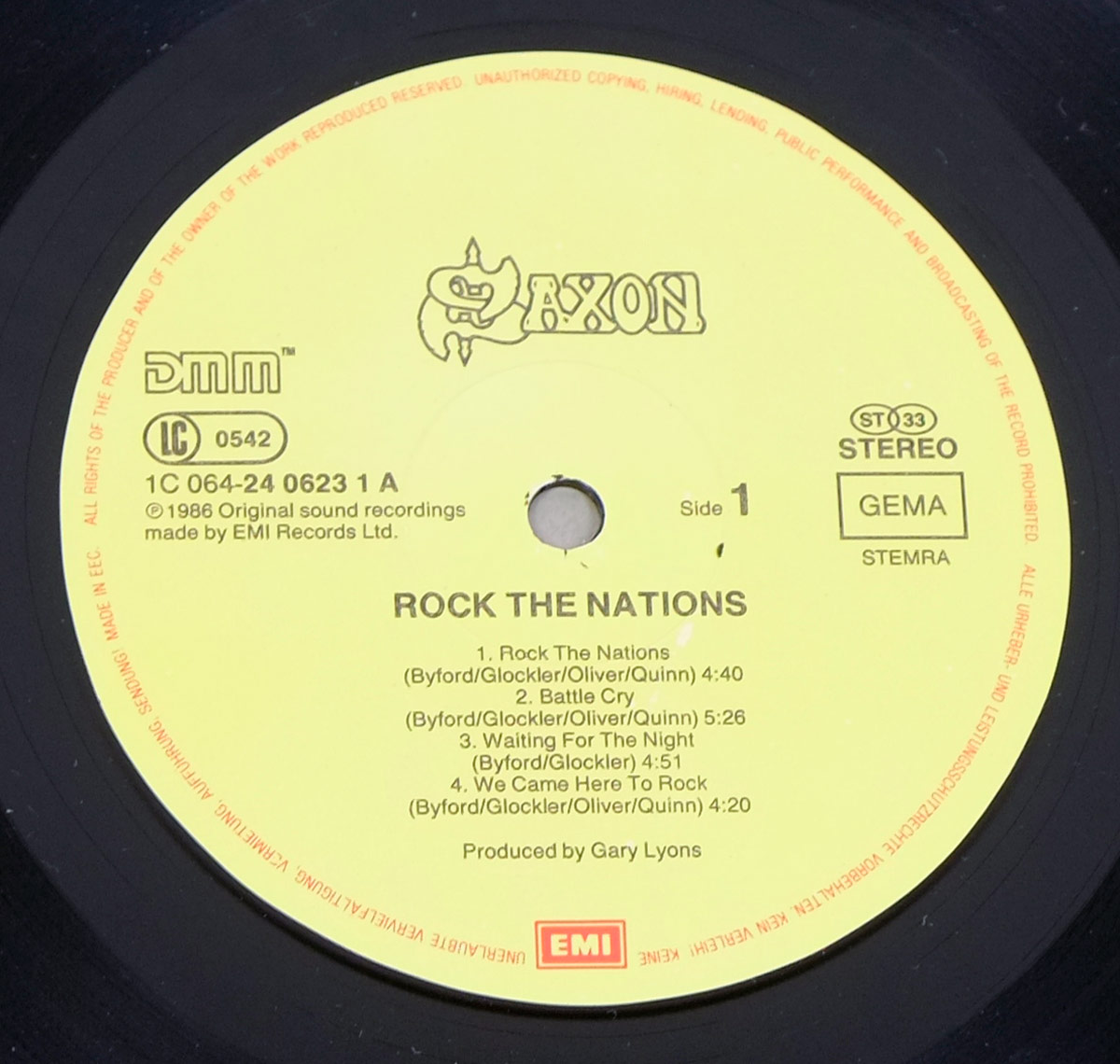 Close-up of Side One of SAXON's Rock The Nations LP label. The label is yellow with black text, showing the tracklist for Side 1, band name, EMI logo, DMM logo, catalog number 1C 064-24 0623 1 A, and credits.