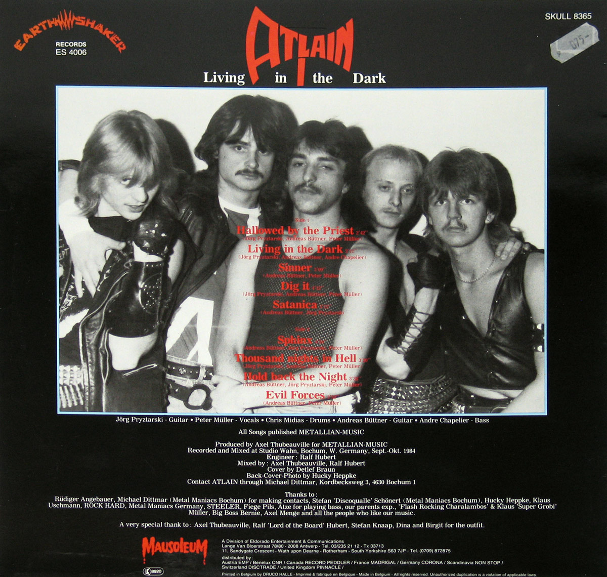Back cover of Atlain’s Living in the Dark album featuring a black-and-white group photo of the band members in classic 1980s heavy metal style, with leather outfits and long hair. Includes the Atlain logo in red, album title in white, production credits, and the Earthshaker Records and Mausoleum Records logos https://vinyl-records.nl 