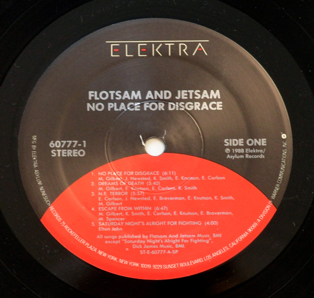 Side One of Flotsam and Jetsam's 'No Place for Disgrace' vinyl record, released under Elektra/Asylum Records. The label features a black background with the Elektra logo at the top, white text displaying the band name and album title, and a red-orange semicircle covering the lower section listing track titles and song credits in white text.