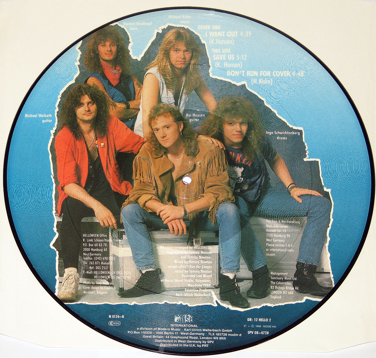 The back side of Helloween’s I Want Out picture disc features a full-color photograph of the band members posed against a deep blue background with a rough, torn-paper effect around the edges. Michael Kiske sits in the center wearing a fringed leather jacket, surrounded by Kai Hansen, Michael Weikath, Markus Grosskopf, and Ingo Schwichtenberg in classic late-’80s metal attire. White text lists the track titles: “I Want Out,” “Save Us,” and “Don’t Run for Cover.” Additional credits and production details are printed at the bottom, reinforcing the disc’s professional yet rebellious design.