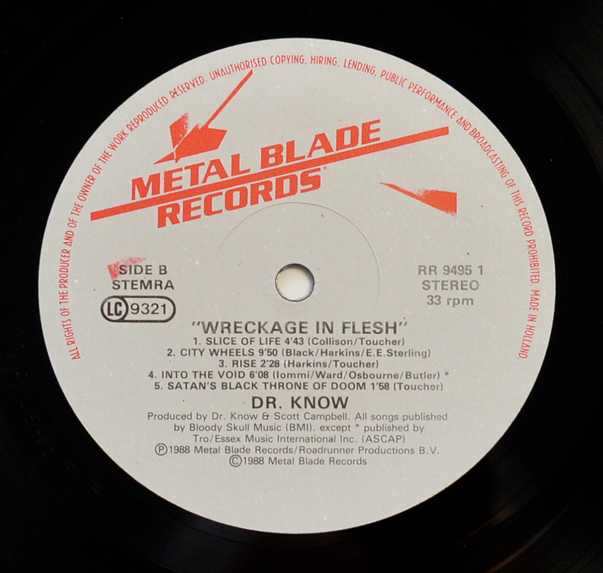 Close-up of Side Two record label of 'Wreckage in Flesh' by Dr. Know. The label is off-white with red 'Metal Blade Records' branding, including the signature blade logo. Side B features five tracks: 'Slice of Life,' 'City Wheels,' 'Rise,' 'Into the Void' (a Black Sabbath cover), and 'Satan's Black Throne of Doom,' with their durations and songwriting credits. The lower section credits Dr. Know and Scott Campbell as producers. Publishing details mention Bloody Skull Music (BMI) and an exception for 'Into the Void,' credited to Essex Music International (ASCAP). The catalog number 'RR 9495 1' and 'Stereo 33 rpm' are also printed. Visit https://vinyl-records.nl