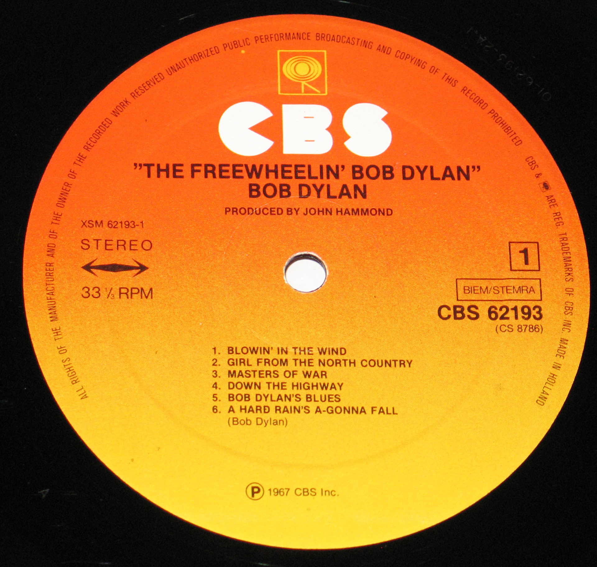 A close-up of the CBS vinyl record label for Bob Dylan's album The Freewheelin' Bob Dylan. The label has an orange-to-yellow gradient with bold white CBS logo at the top, displaying the album title, tracklist, and record details. A central hole is visible.