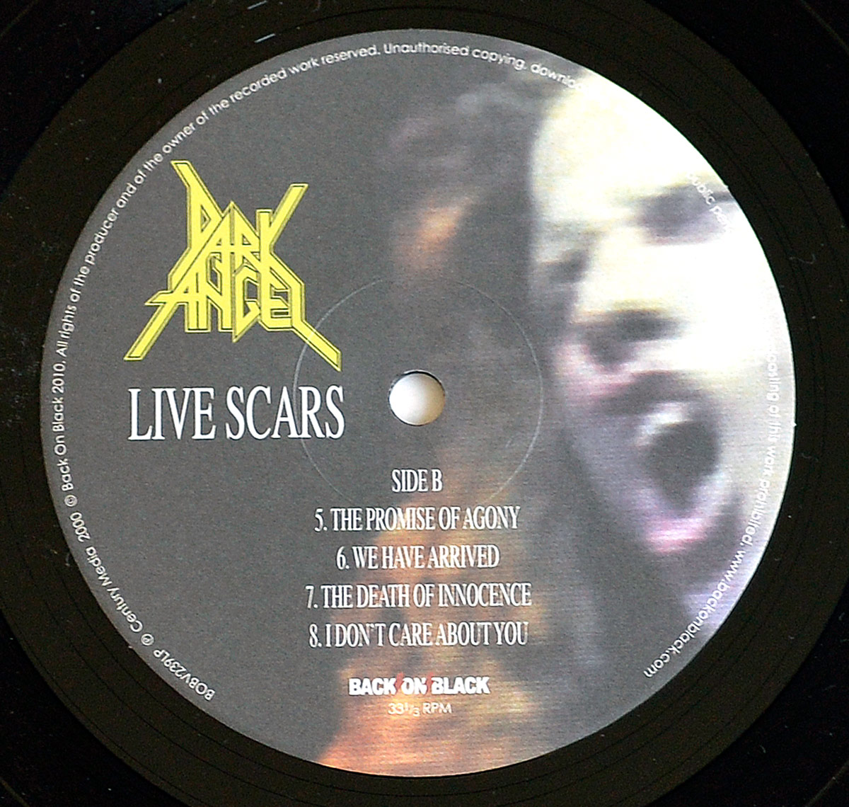 Side B label of Dark Angel's 'Live Scars' 12-inch vinyl record. The label features a blurred, high-contrast close-up of vocalist Ron Rinehart mid-scream. The band's yellow logo is positioned in the upper left, with 'Live Scars' in bold white text below. The tracklist for Side B is centered in white serif font, and 'Back On Black' branding is present at the bottom.