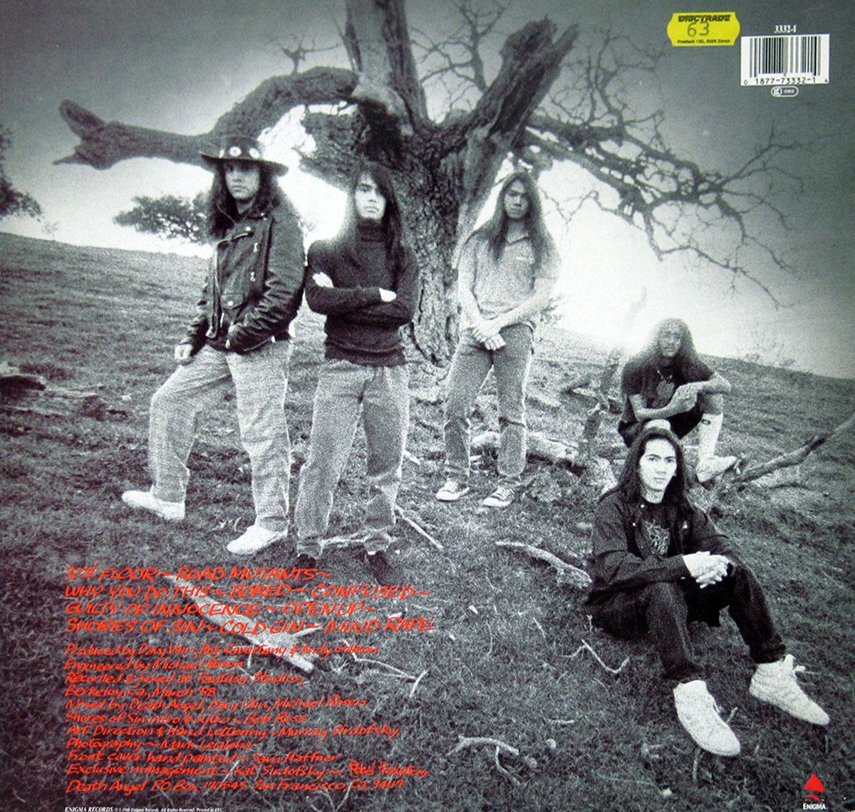 Back cover of Death Angel’s album Frolic Through the Park. The black-and-white photograph shows the five band members standing and sitting around a large, bare tree in an open field. Two members stand with arms crossed, one leans against the tree, one sits on a branch, and one crouches in the foreground. The tracklist is written in bold red, handwritten-style text across the bottom left, with production credits listed beneath it. The somber and raw imagery reflects the album’s thrash metal aesthetic.