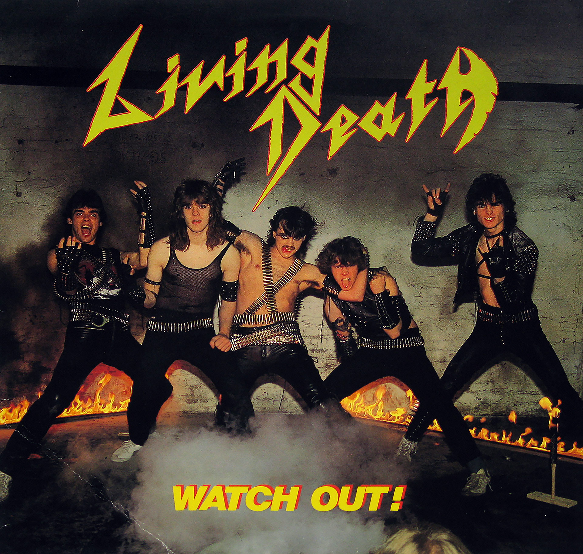 Album cover of “Watch Out!” by Living Death featuring the band members dressed in spiked and studded leather outfits, posing in an industrial setting with flames on the floor, sharp jagged band logo in yellow and red, and album title in bold yellow text.