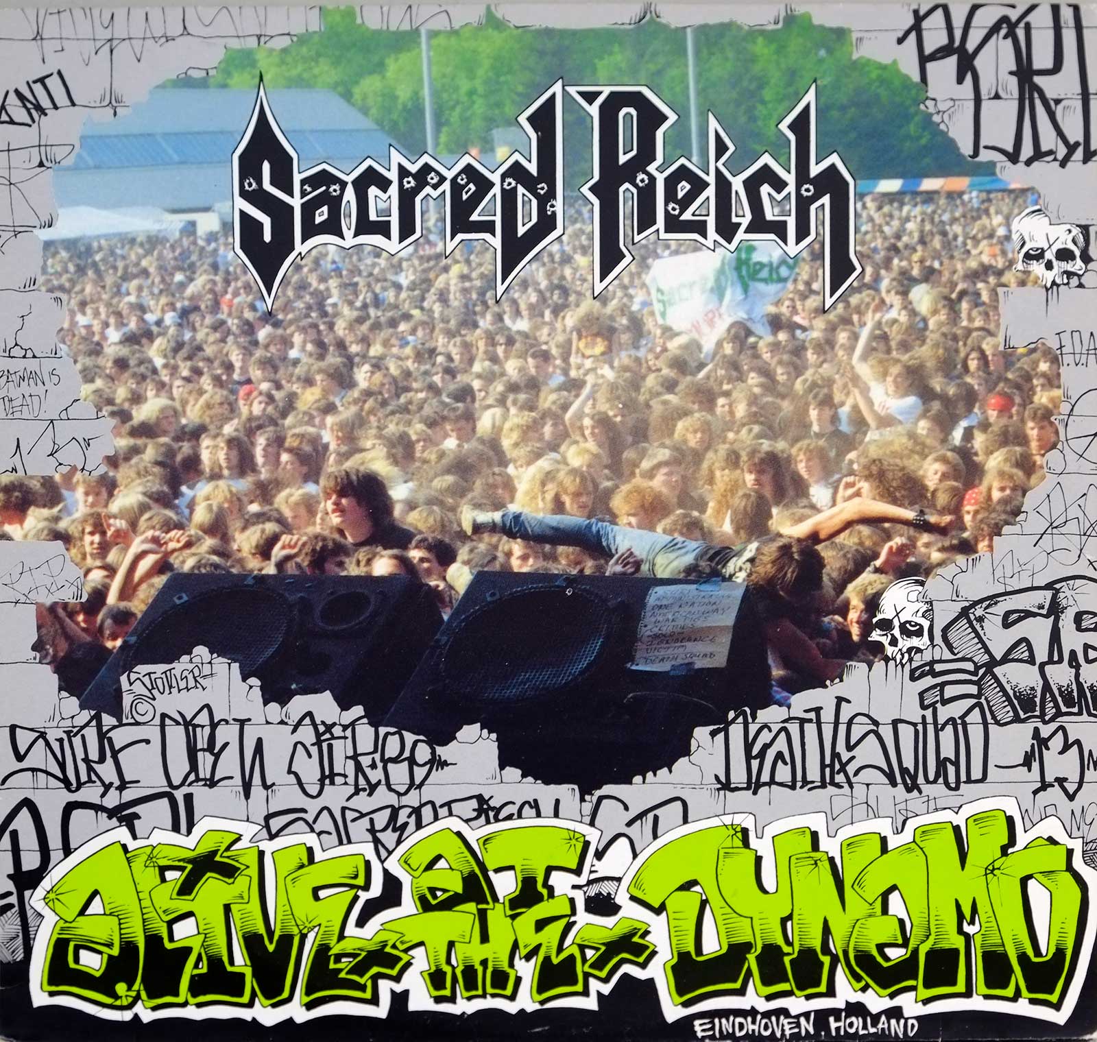 lbum cover for Sacred Reich's 'Alive at Dynamo' featuring a large, energetic crowd at the Dynamo Open Air Festival in Eindhoven, Netherlands. The cover shows the band's name in bold, metallic font at the top, with a graffiti-inspired border around the photo. The album title 'Alive at Dynamo' appears in vibrant green graffiti-style text at the bottom. A fan is crowd-surfing toward the stage, capturing the intense energy of a live metal concert.