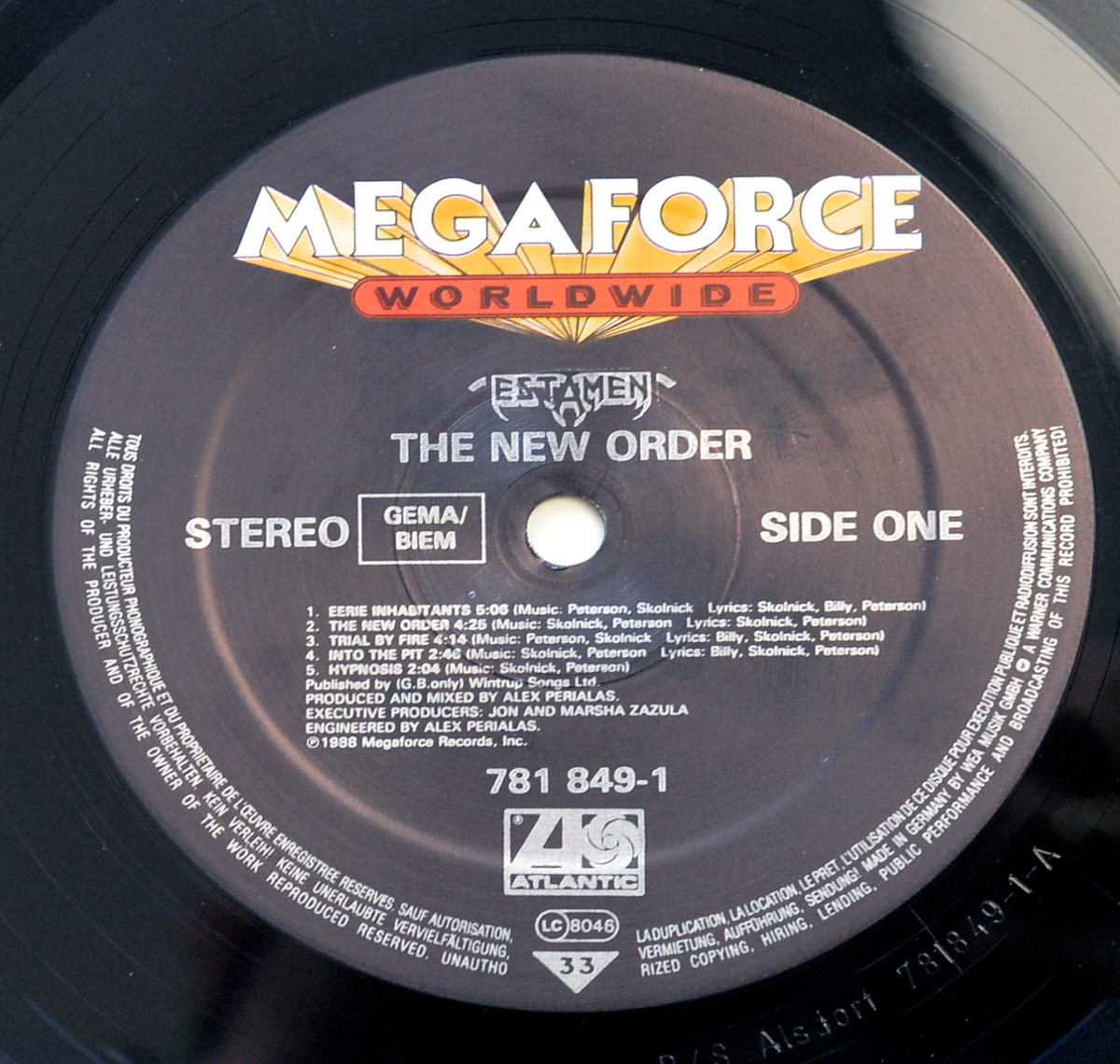Close-up of the record label on Testament's 'The New Order' vinyl, featuring a black background with silver text and the Megaforce Worldwide logo in bold white and red at the top. The label displays the album title, band name, tracklist for Side One, and production credits, encircling the vinyl's central spindle hole.