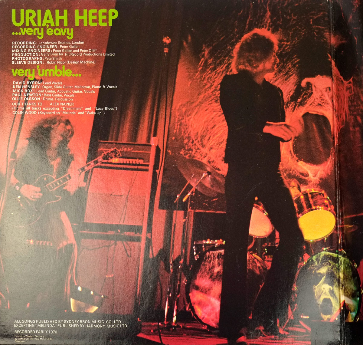 Inner gatefold cover of Uriah Heep's 'Very 'Eavy... Very 'Umble' (German Release), featuring a dramatic red-lit live performance with the band playing onstage, framed by a massive eerie face in the background and drumheads reflecting the album artwork.